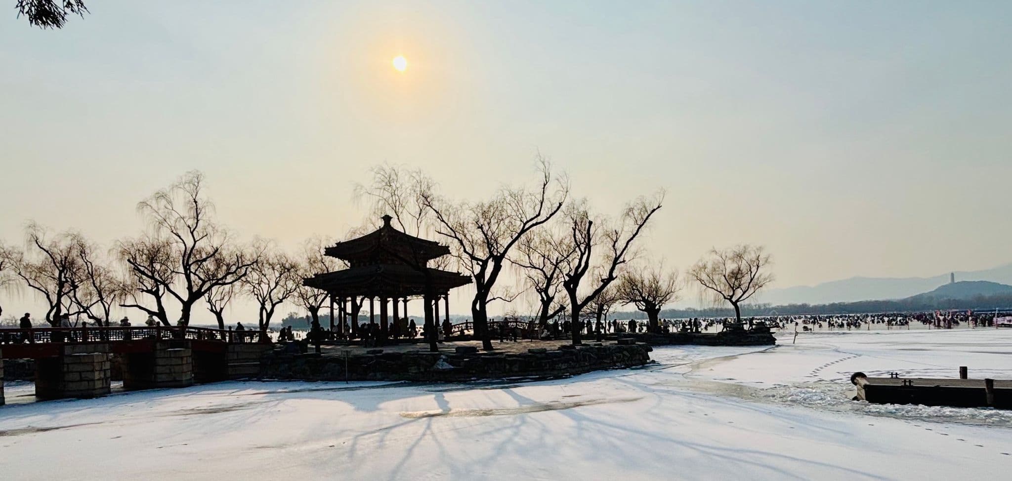 Summer Palace pavilion silhouetted against the sun with willow trees and a frozen lake in Beijing, China.