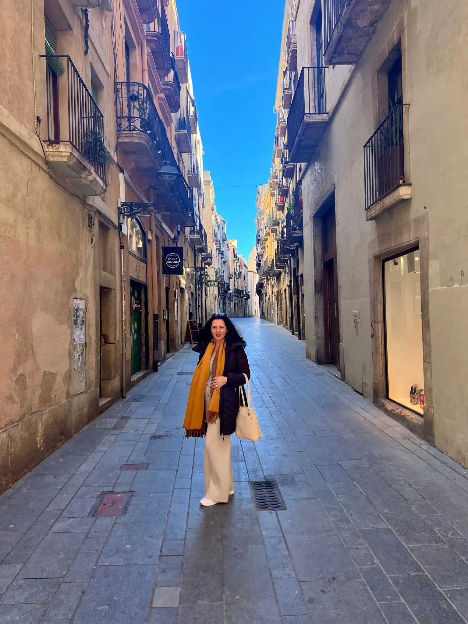 Narrow historic street in Tarragona Old Town, Spain with a woman standing in the center wearing a yellow scarf and holding a bag.