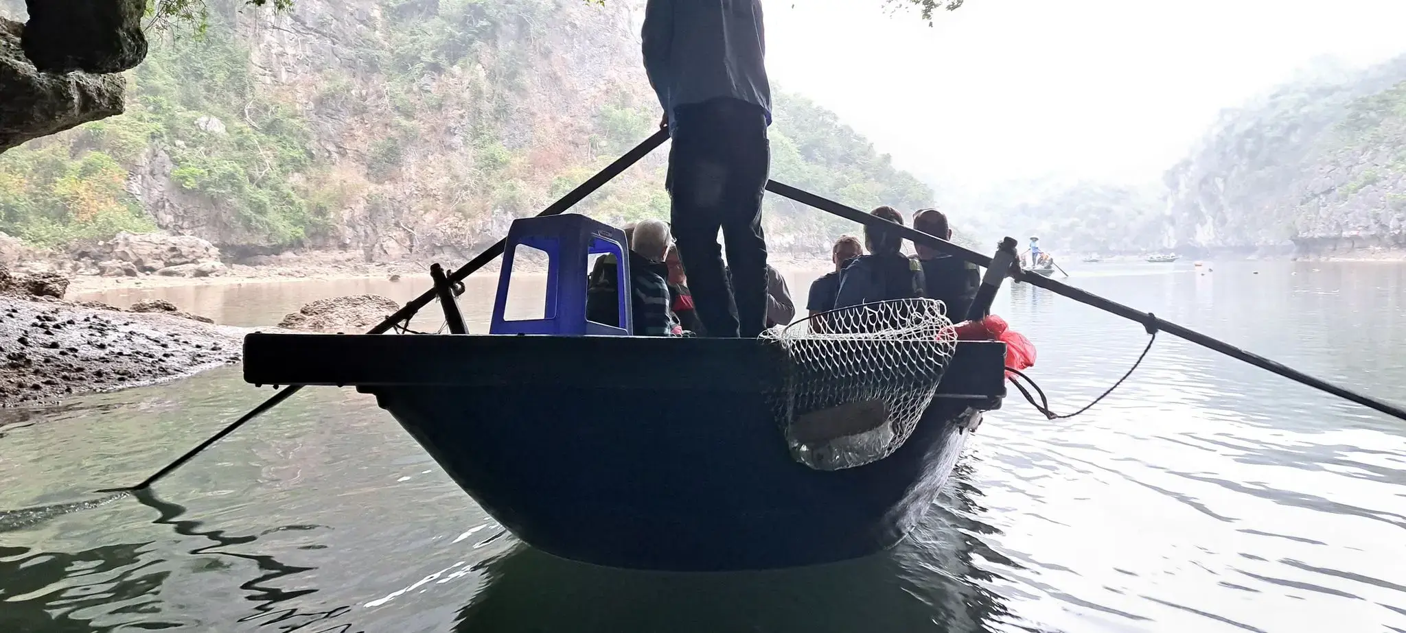 Rowboat with passengers being rowed under a rock arch into a lagoon in Ha Long Bay, Vietnam.