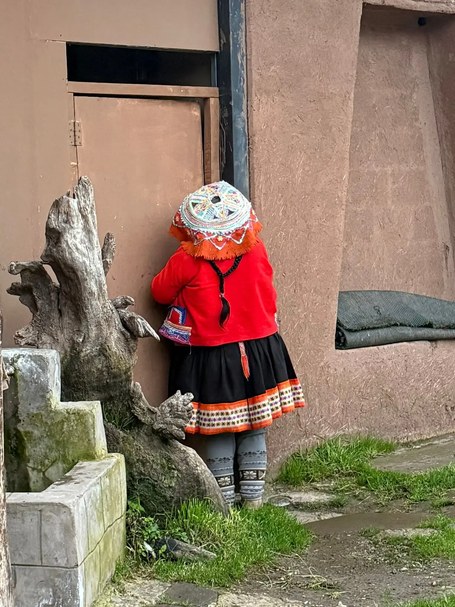 Person in a red jacket and embroidered hat standing at a doorway in the Sacred Valley, Cusco, Peru.