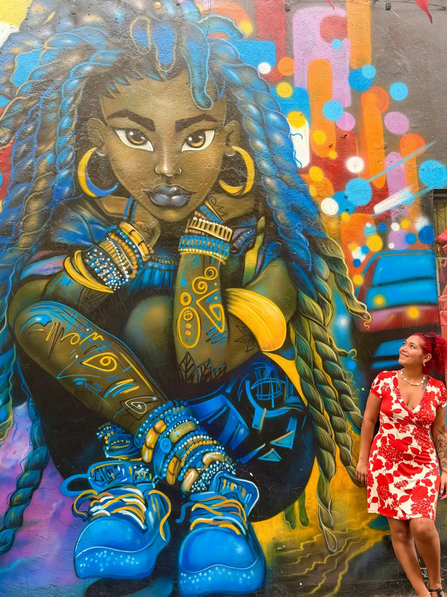 Large colorful mural of a woman with blue braids beside a traveler in a red floral dress, Getsemaní, Cartagena, Colombia