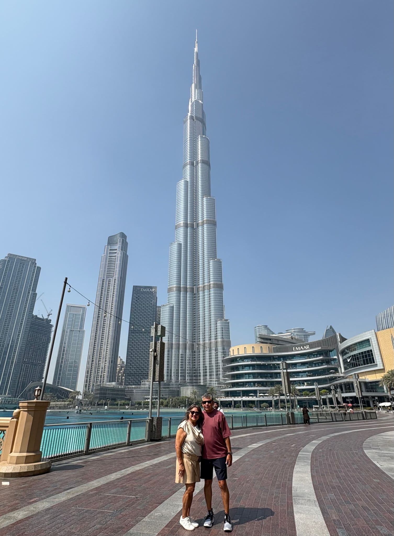 Burj Khalifa towering over a couple posing on the Downtown Dubai waterfront promenade, United Arab Emirates.