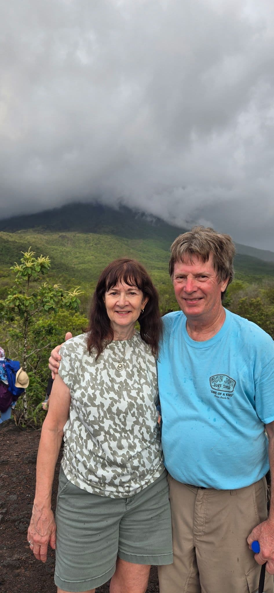 Arenal Volcano shrouded in clouds with a smiling couple posing on volcanic slopes in La Fortuna, Costa Rica.