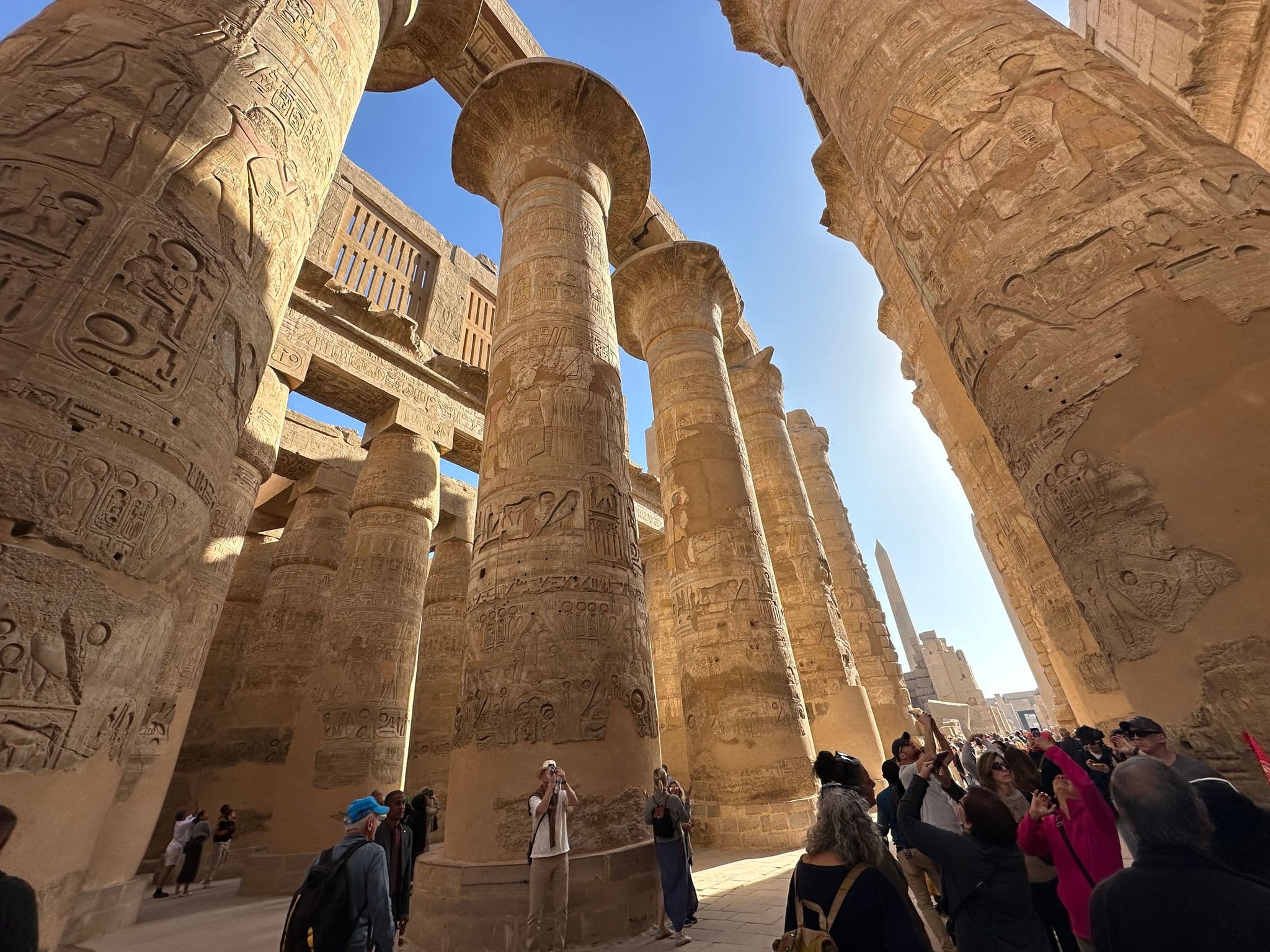 Tall carved columns of the Great Hypostyle Hall at Karnak Temple in Luxor, Egypt, with tourists taking photos among the pillars.