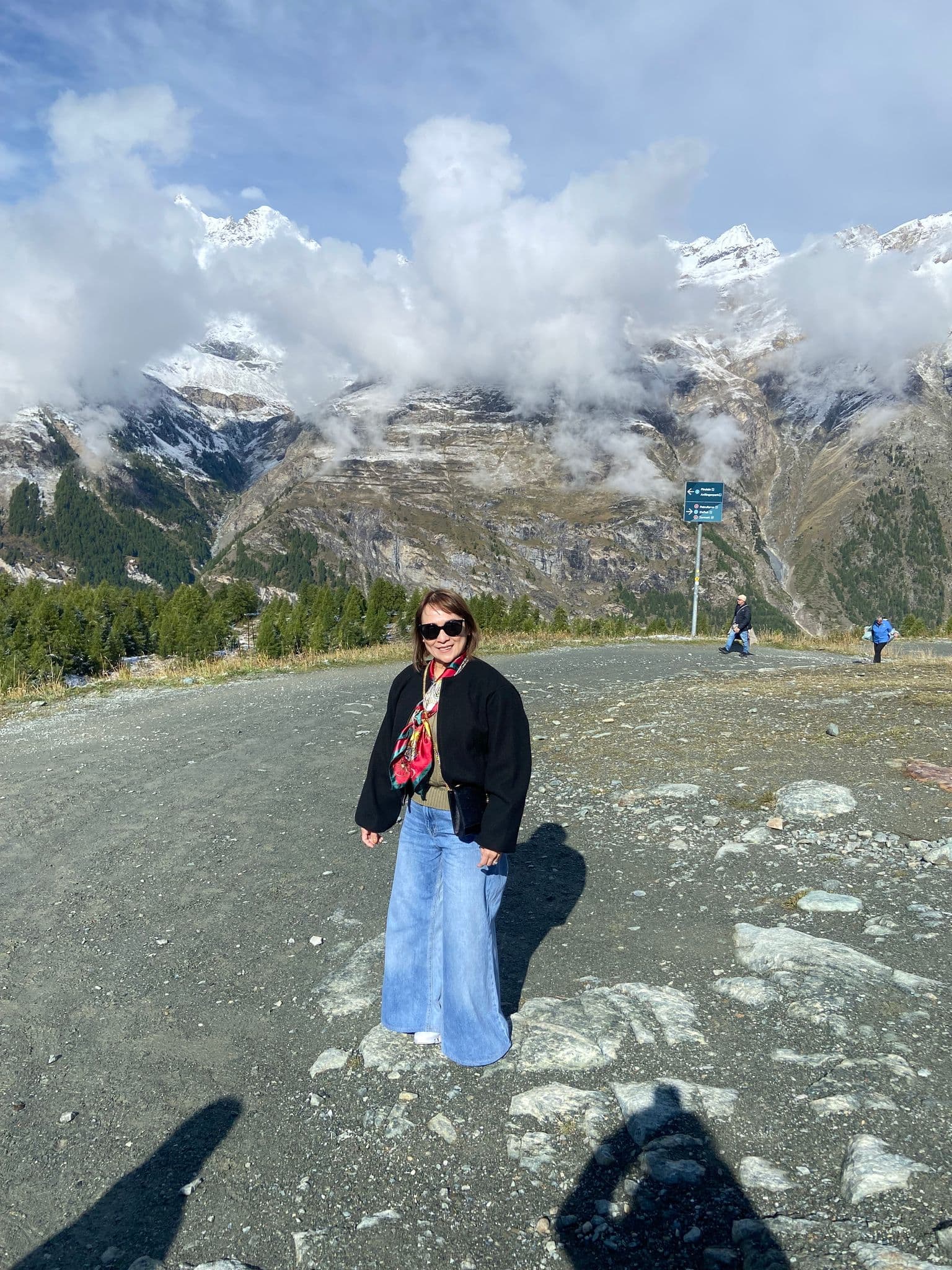 Snow-capped Matterhorn and alpine slopes with a person standing on a gravel viewpoint in Zermatt, Switzerland.