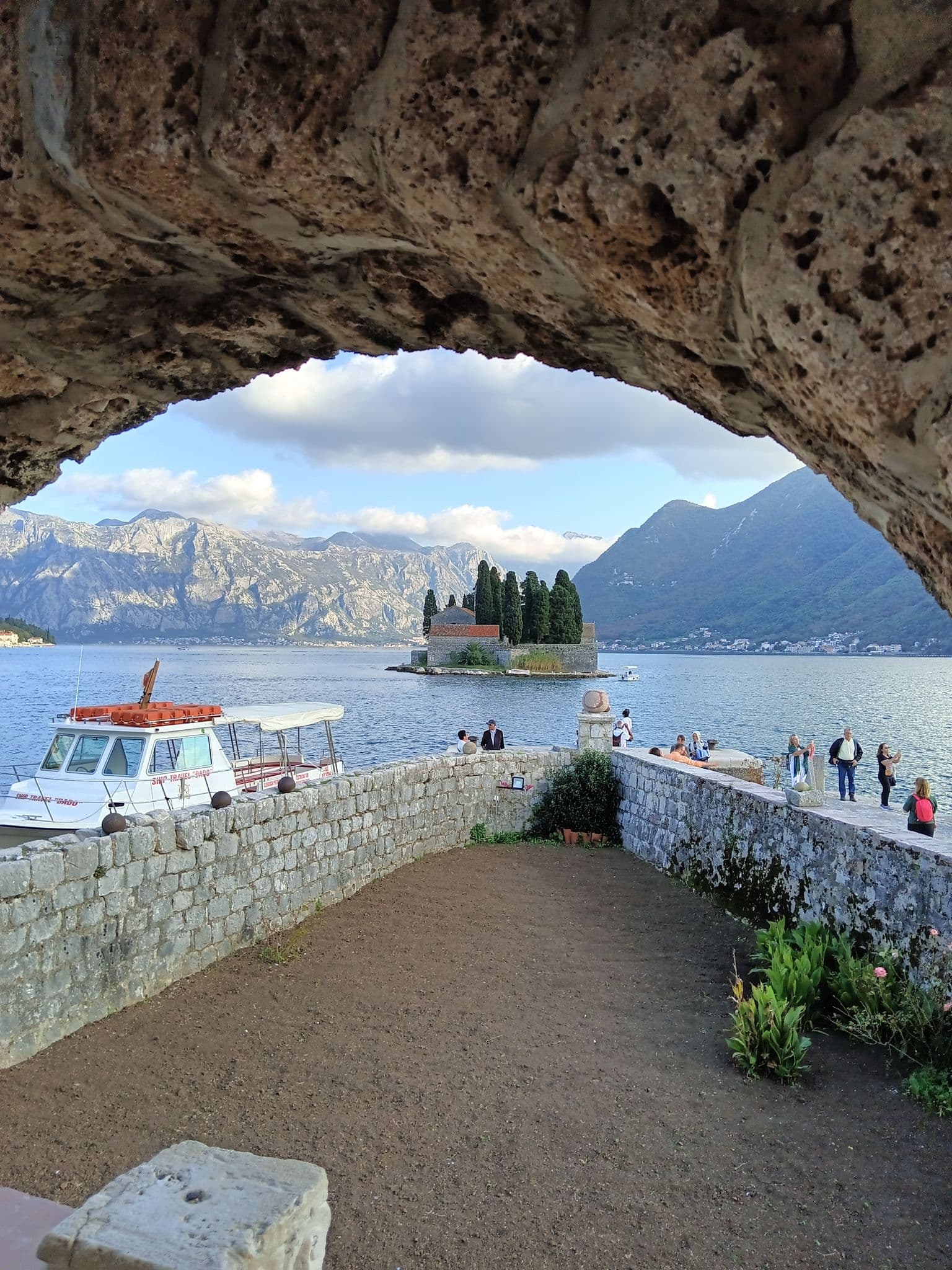 Our Lady of the Rocks island off Perast with a small boat at the quay and people on the stone pier, Bay of Kotor, Montenegro.