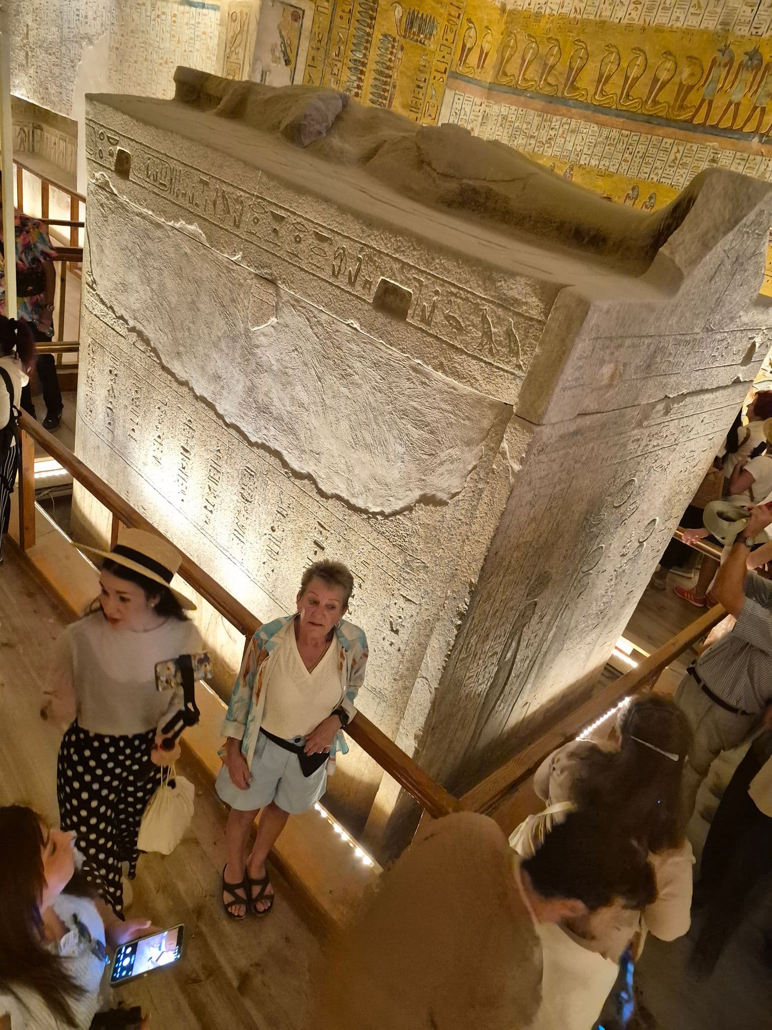 Ancient stone sarcophagus with hieroglyphs inside a tomb at the Valley of the Kings, Egypt, with tourists looking around.