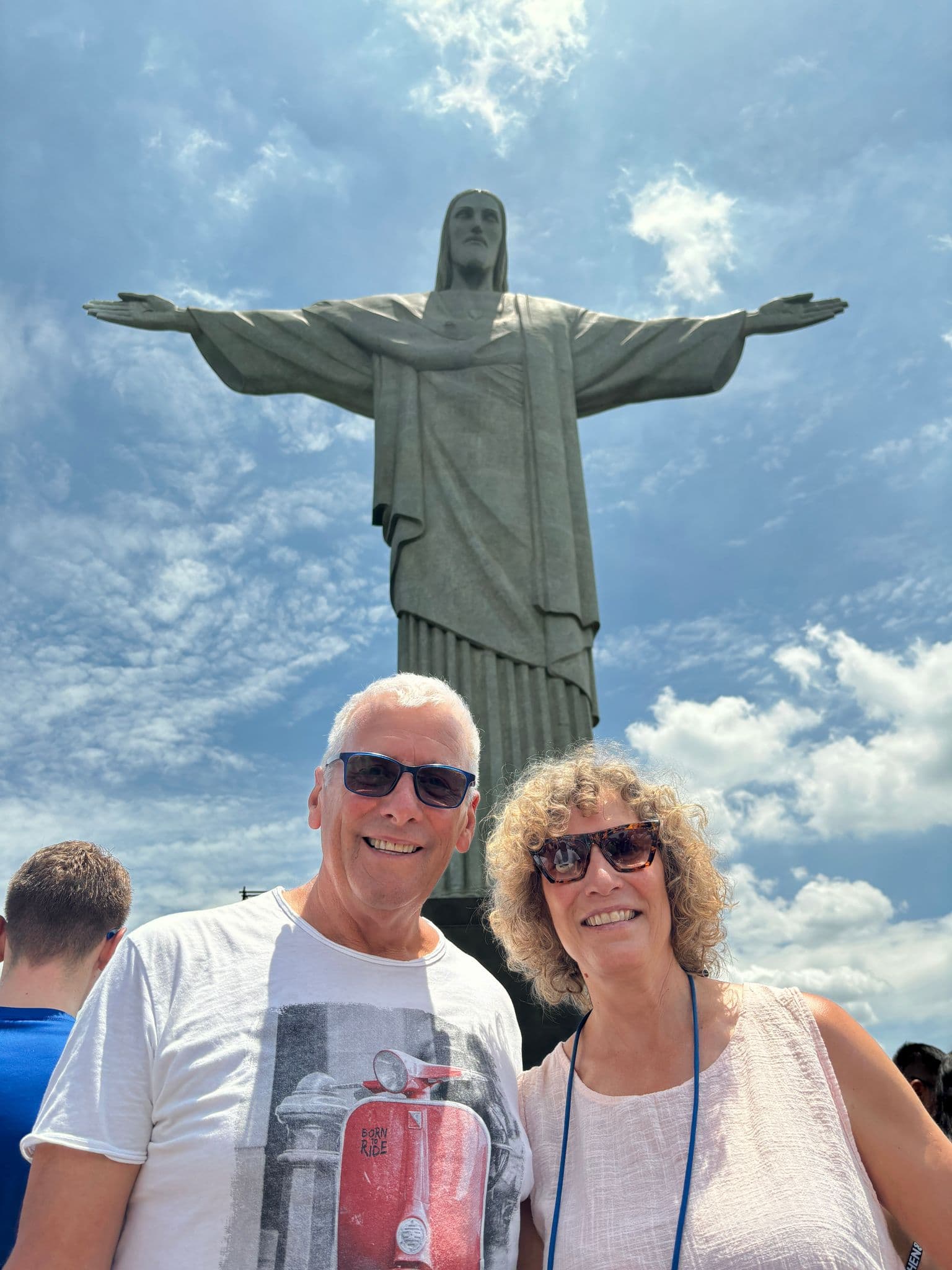 Christ the Redeemer on Mount Corcovado with a smiling couple in sunglasses in the foreground, Rio de Janeiro, Brazil