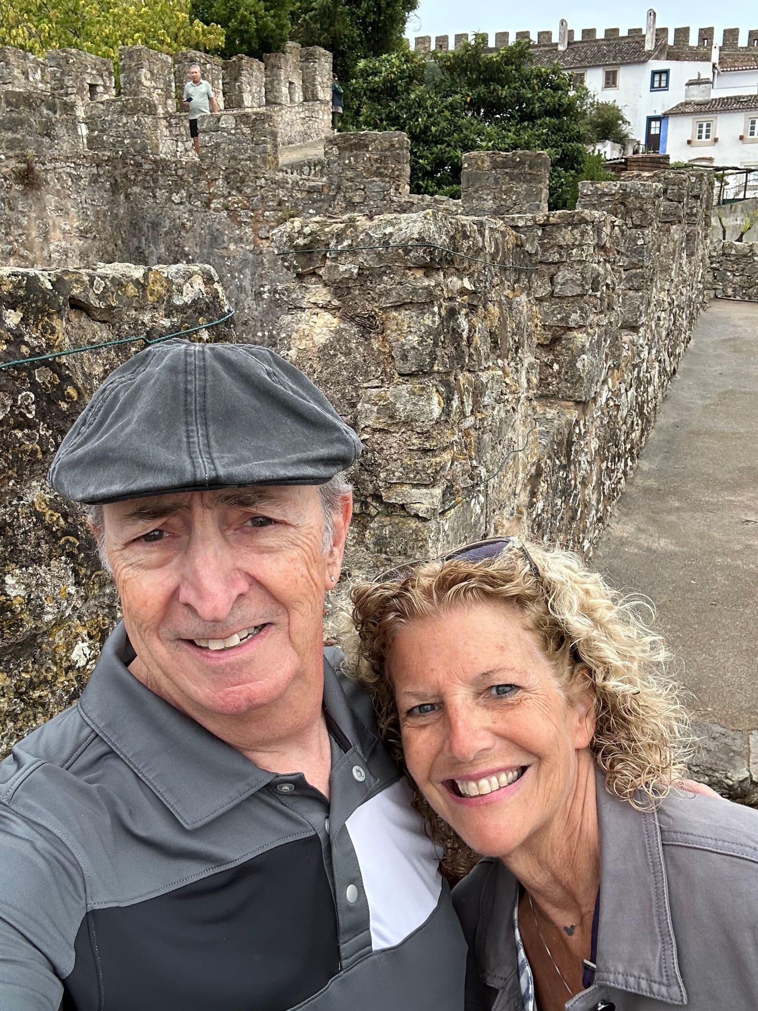 Óbidos Castle walls with two travelers taking a selfie on the upper ramparts in Óbidos, Portugal.