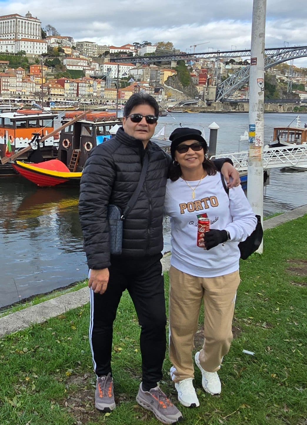 Dom Luís I Bridge and the Douro River with two travelers posing on the riverside in Porto, Portugal.