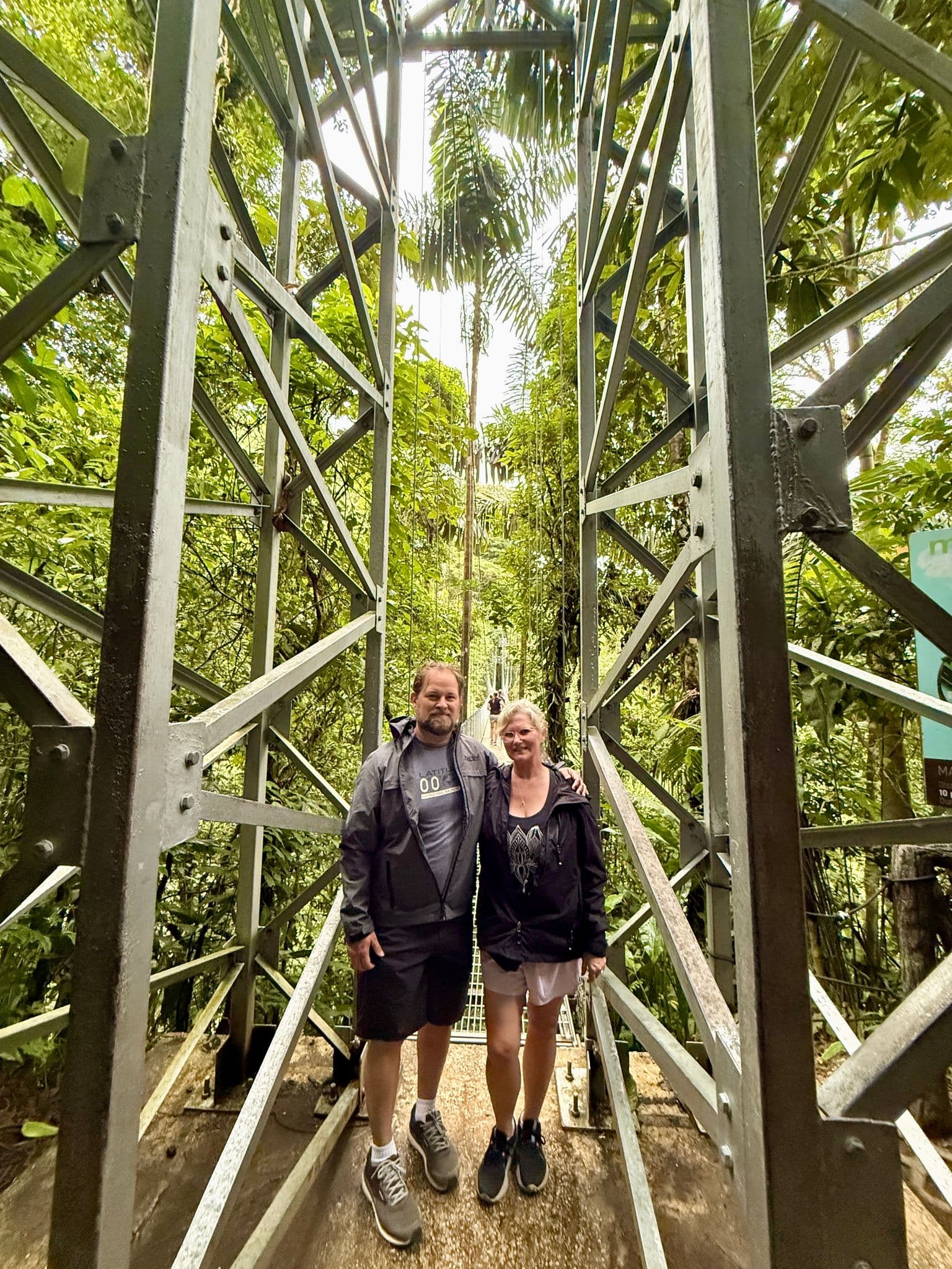 Couple standing on a metal hanging bridge amid dense cloud forest vegetation in Costa Rica.