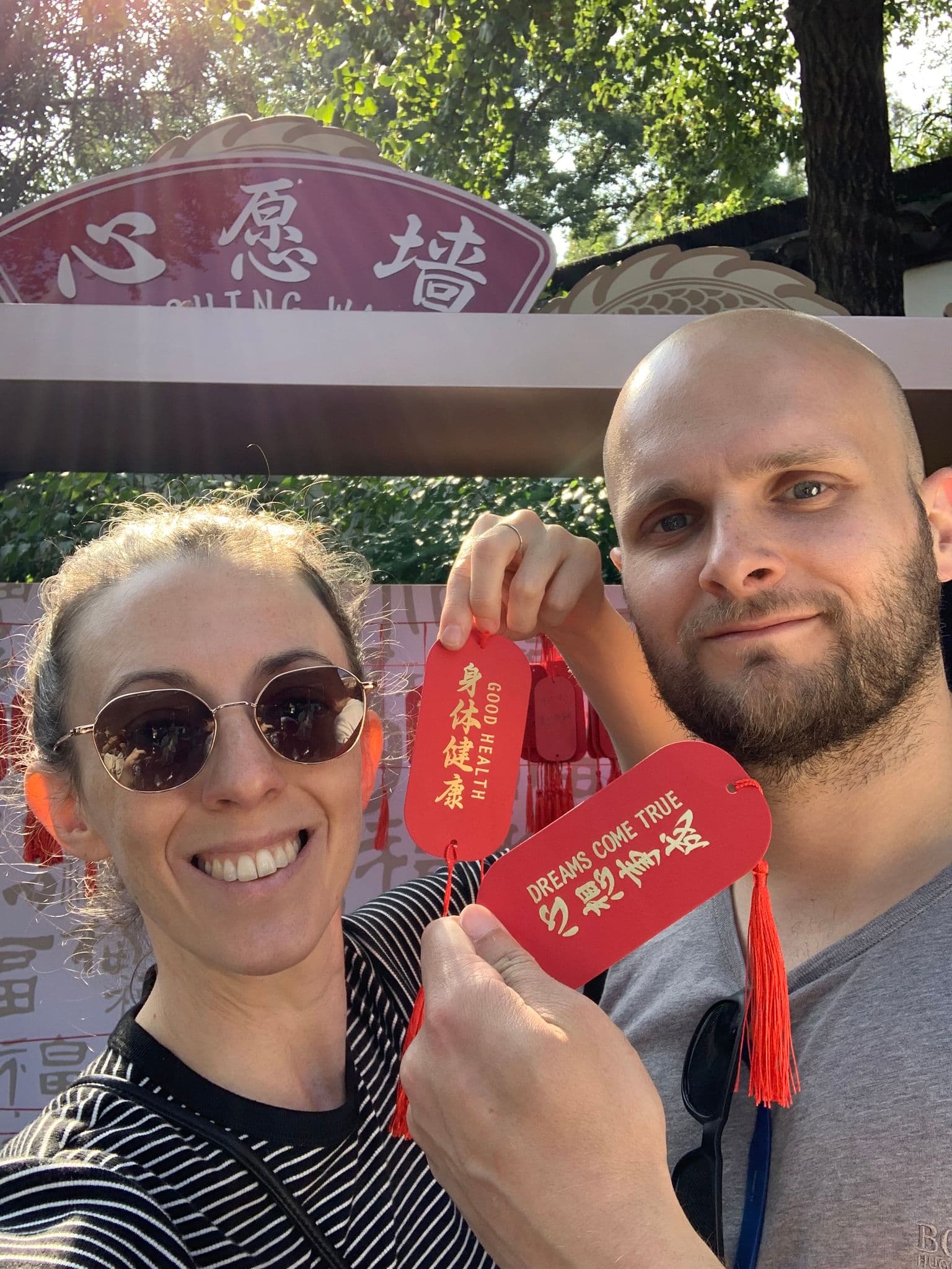 Yuyuan Garden wishing wall in Shanghai, China with two travelers holding red wish plaques reading Dreams Come True.