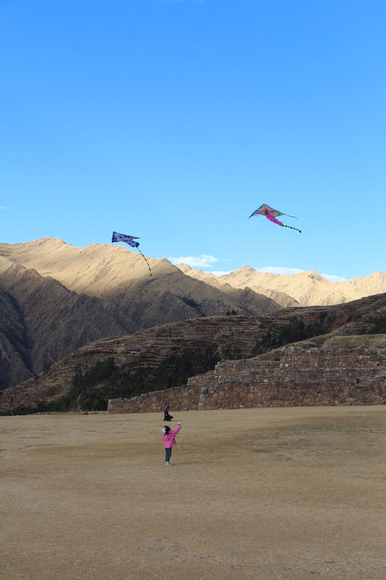 Chinchero archaeological terraces with colorful kites flying overhead and a child holding a kite on the field, Sacred Valley, Peru.
