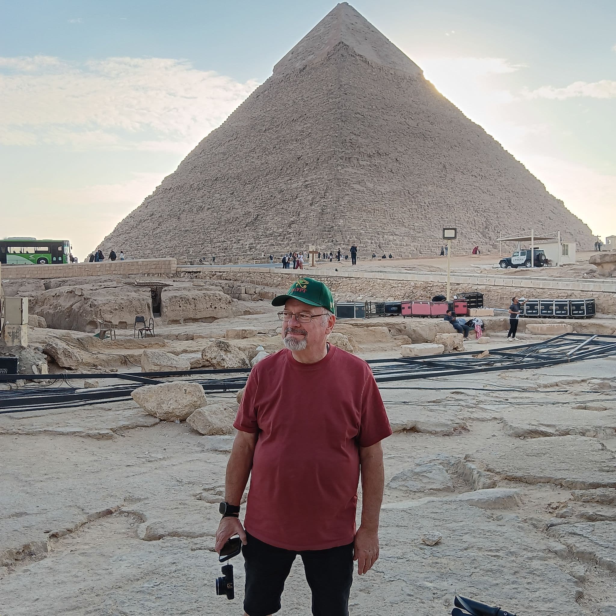 Great Pyramid of Giza towering behind a man standing and holding a camera on a trip in Giza, Egypt.
