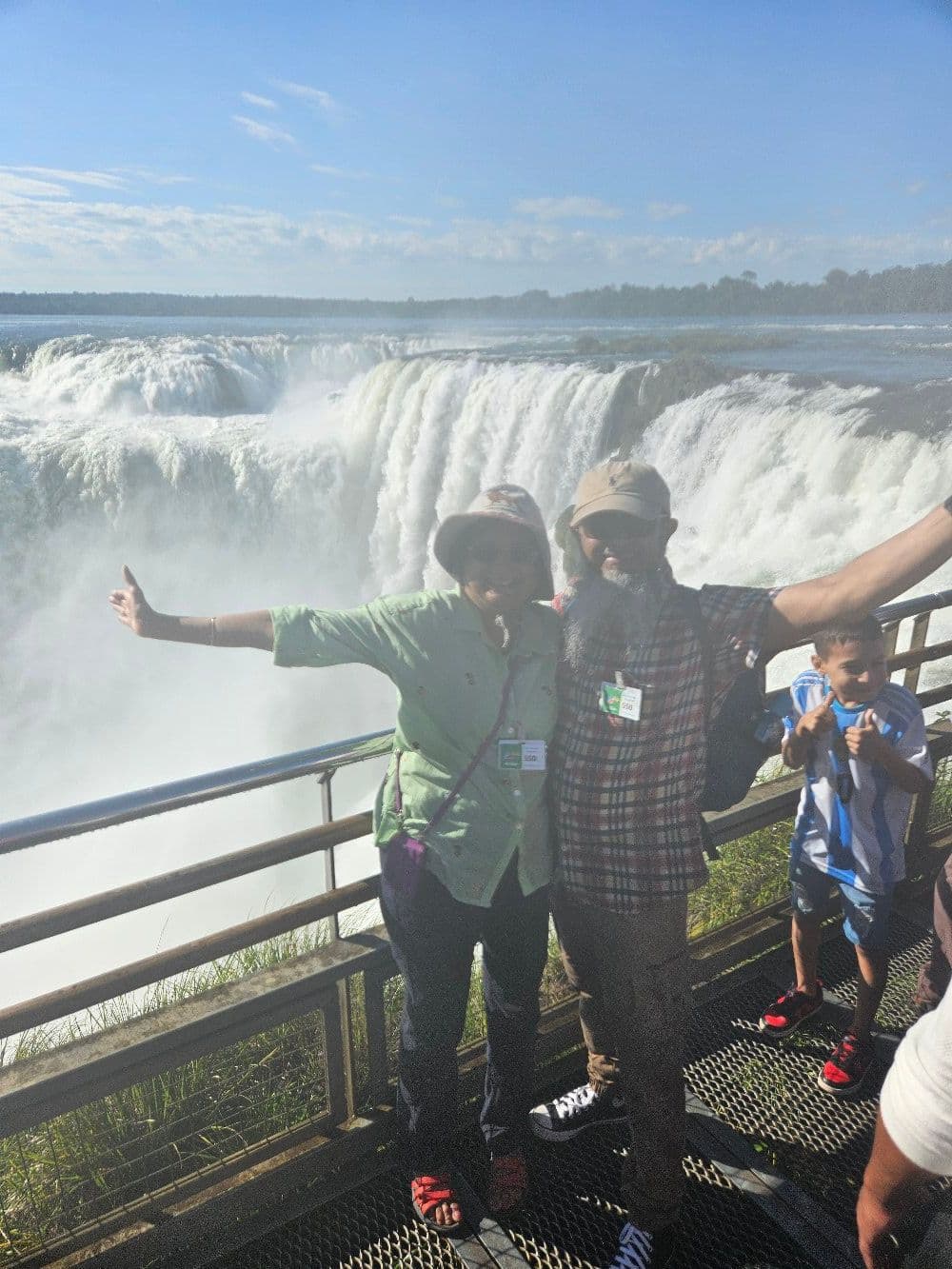 Garganta del Diablo at Iguazu Falls with two travelers posing on a metal viewing platform in Iguazú National Park, Argentina.