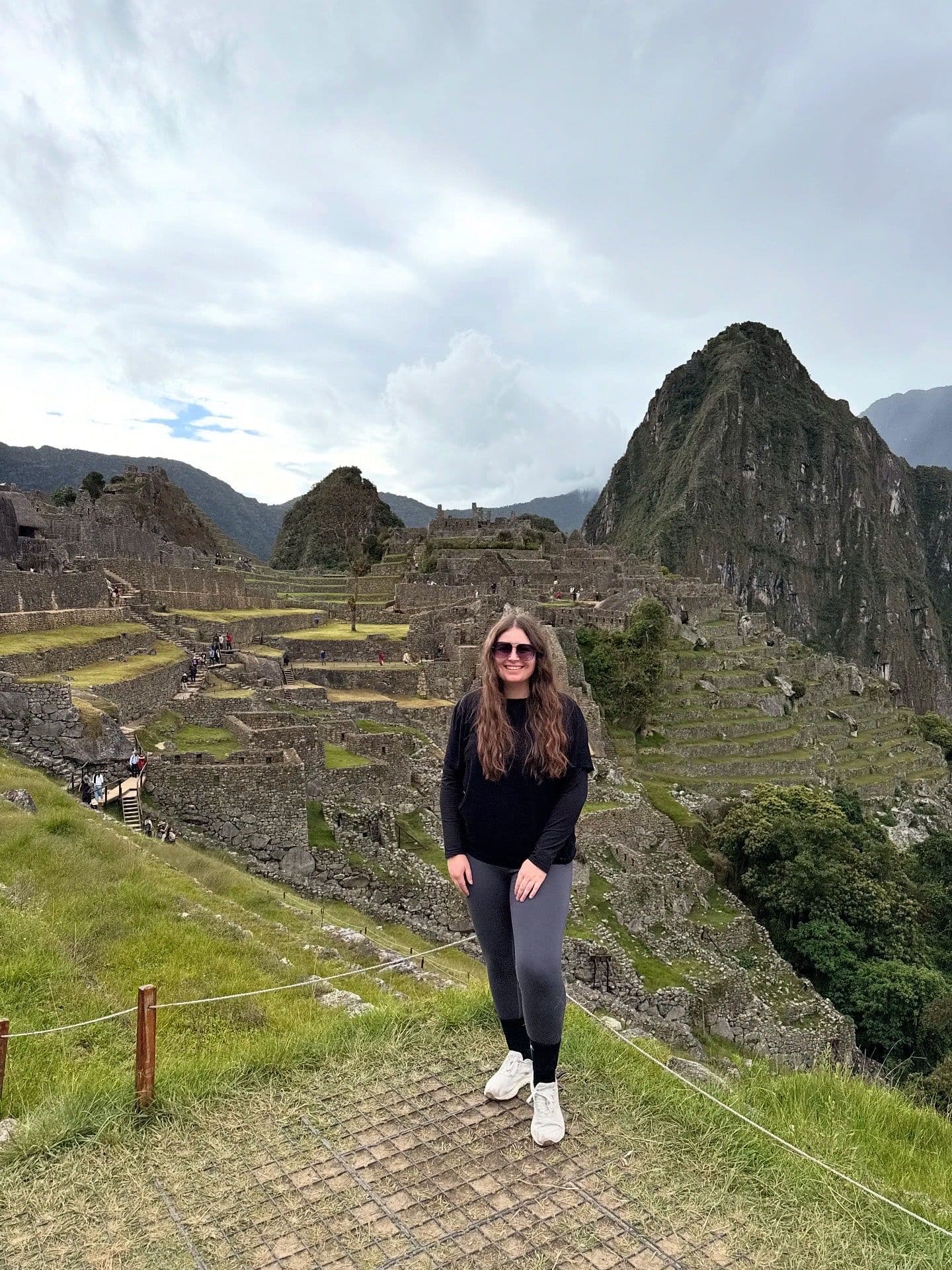 Machu Picchu ruins with a traveler standing on a grassy terrace posing for a photo, Cusco region, Peru.