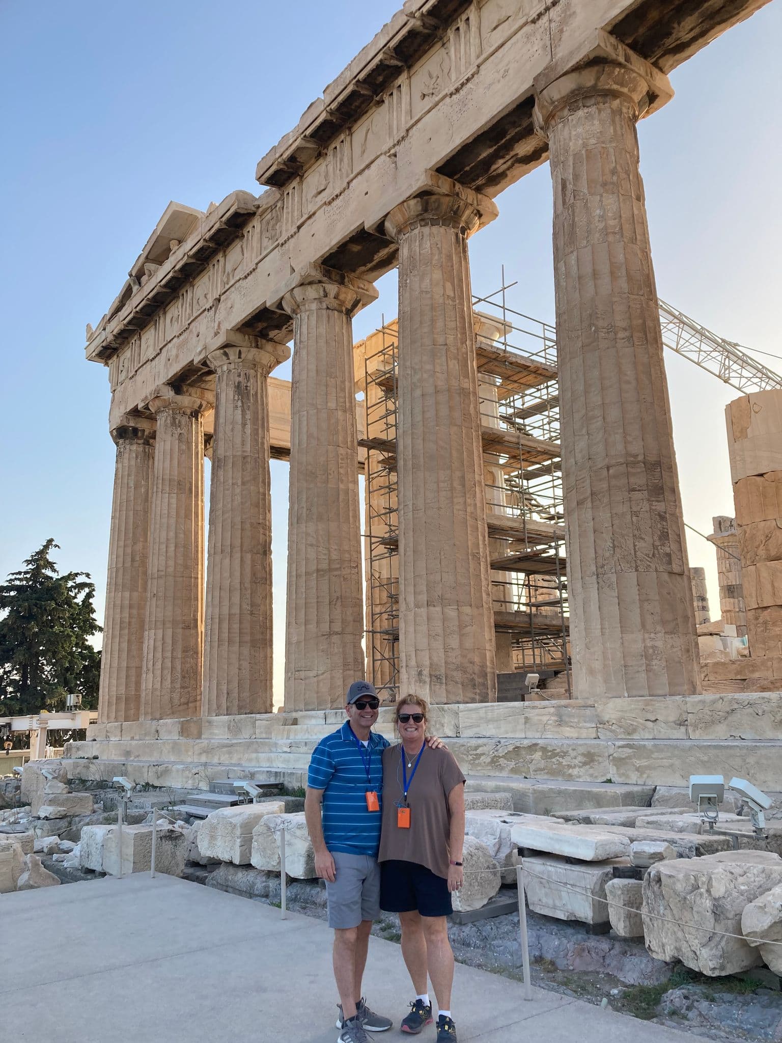 Parthenon at the Acropolis with two travelers posing in front on a clear day in Athens, Greece.