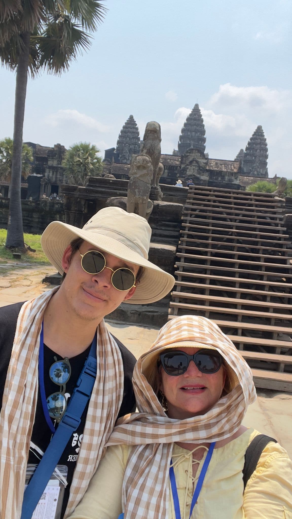 Angkor Wat temple in Siem Reap, Cambodia with two travelers taking a selfie on the front steps.