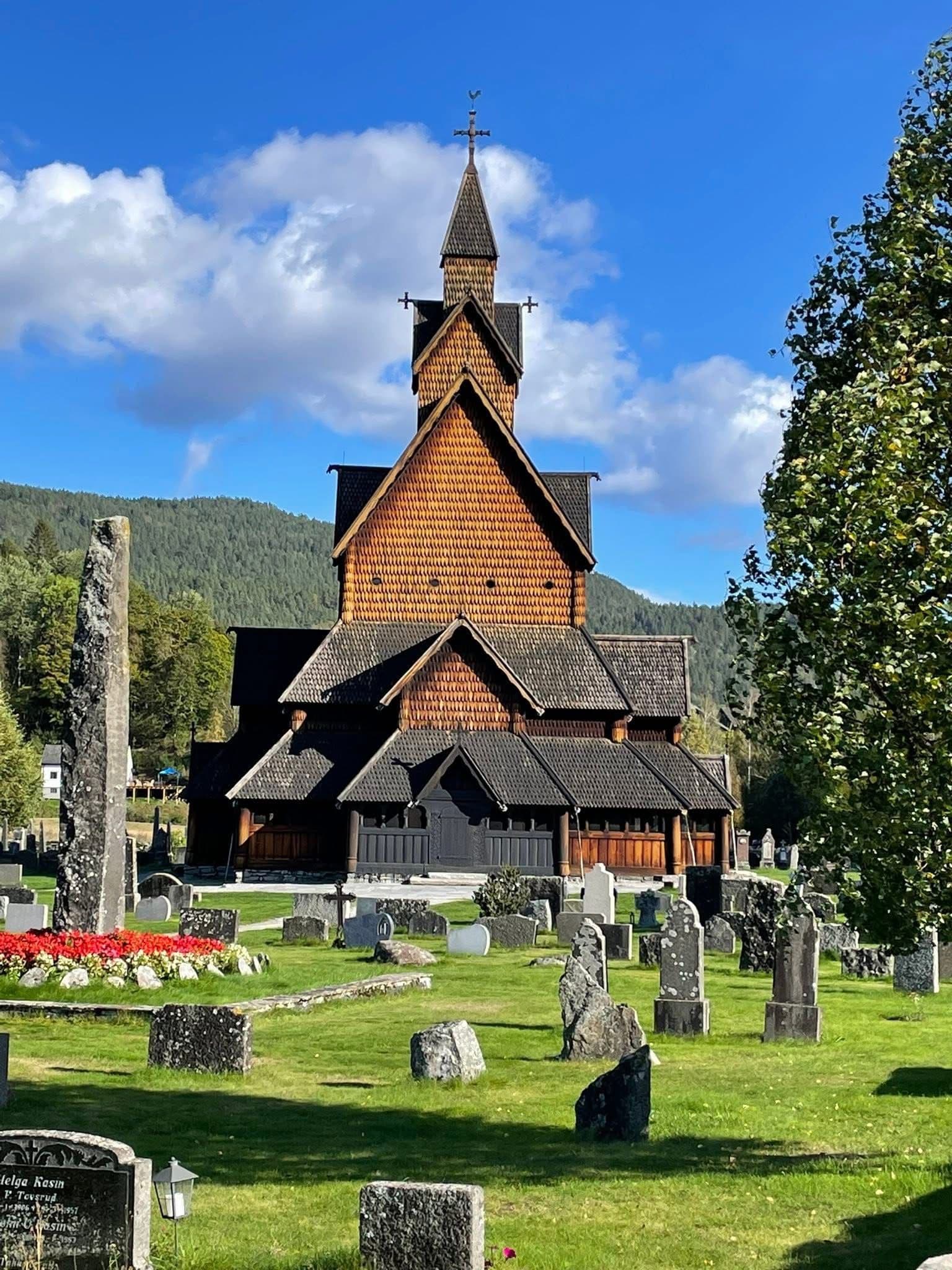 Reinli Stave Church standing behind a grassy churchyard dotted with tombstones in Reinli, Norway.