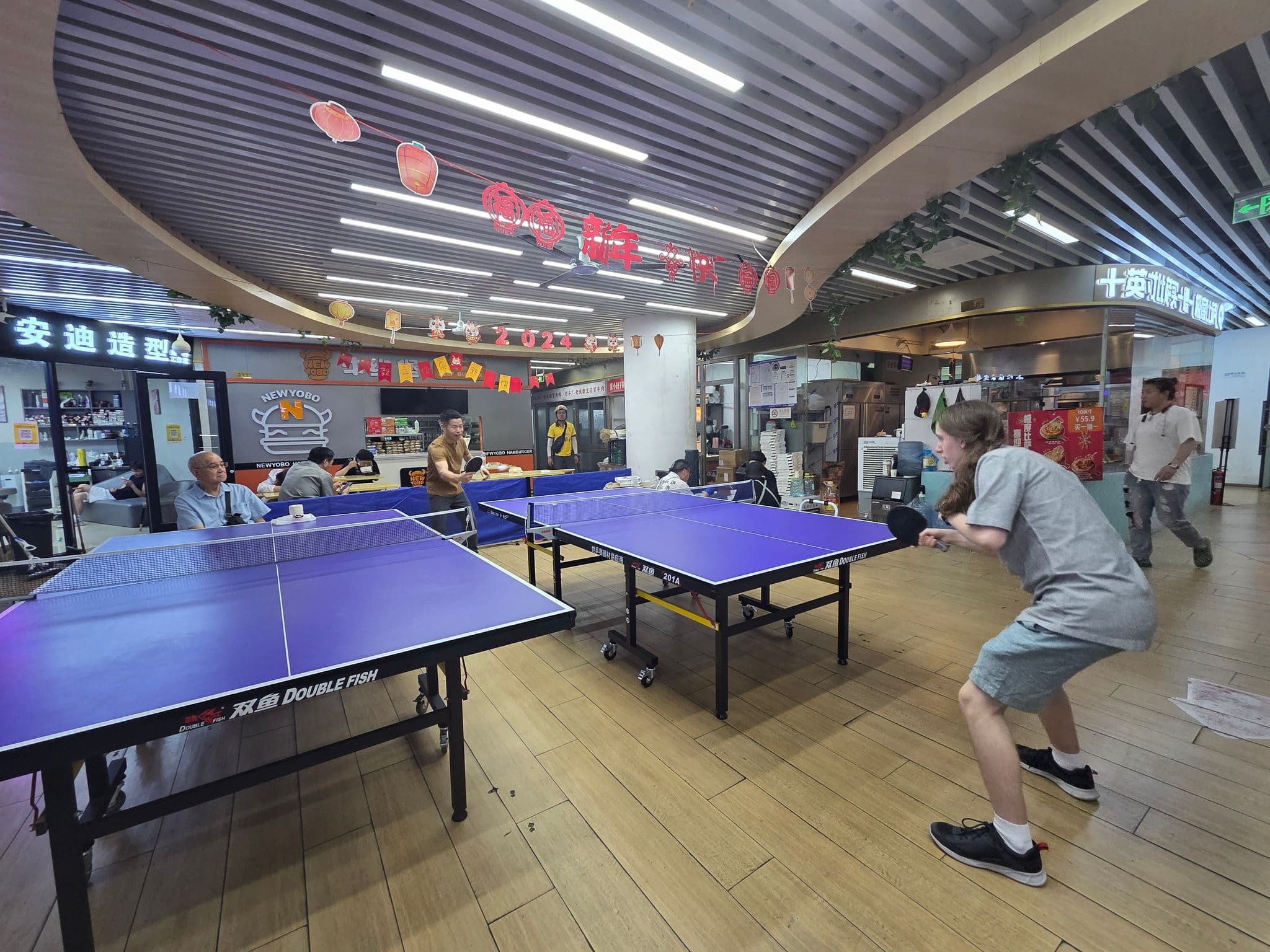 Table tennis tables with local players and a visitor playing inside a shopping centre in Beijing, China.
