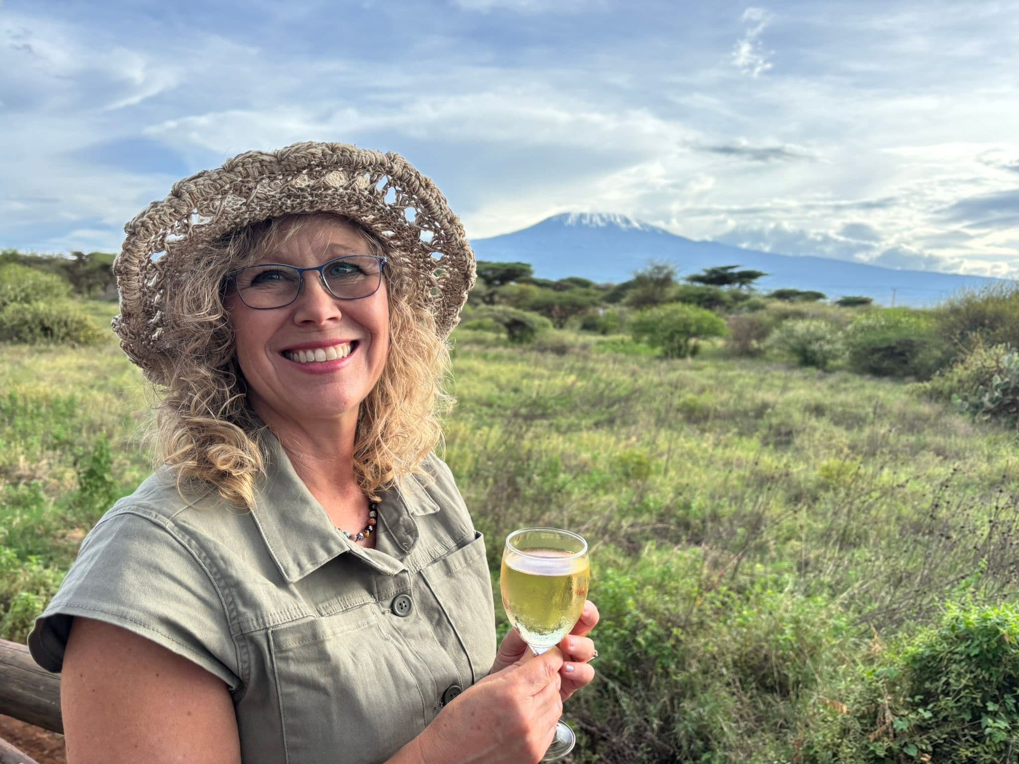 Mount Kilimanjaro framed behind a smiling woman holding a glass of wine on a viewing platform in Amboseli, Kenya.
