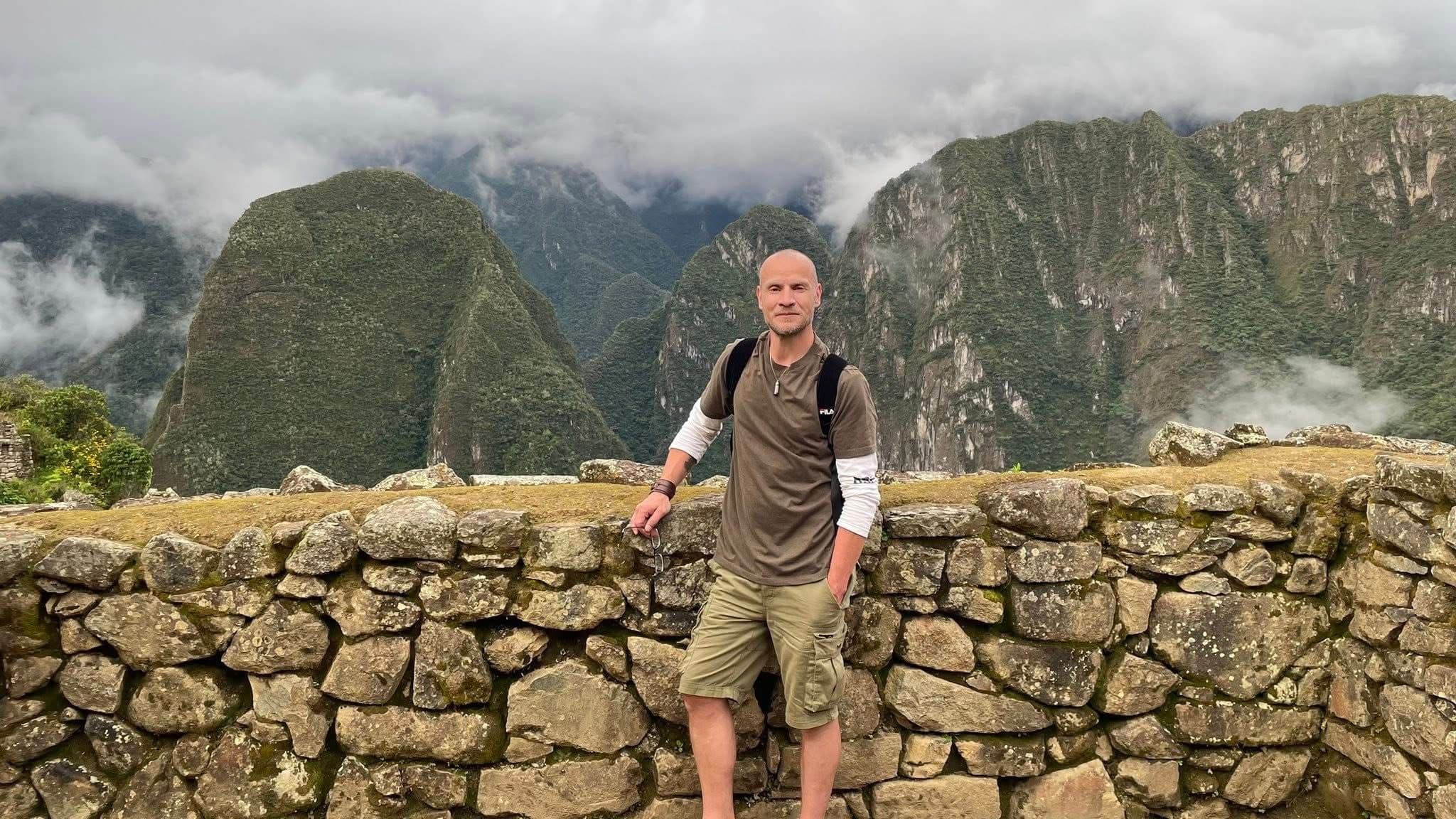 Machu Picchu stone wall and Andes peaks with a traveler leaning on the wall, Cusco region, Peru