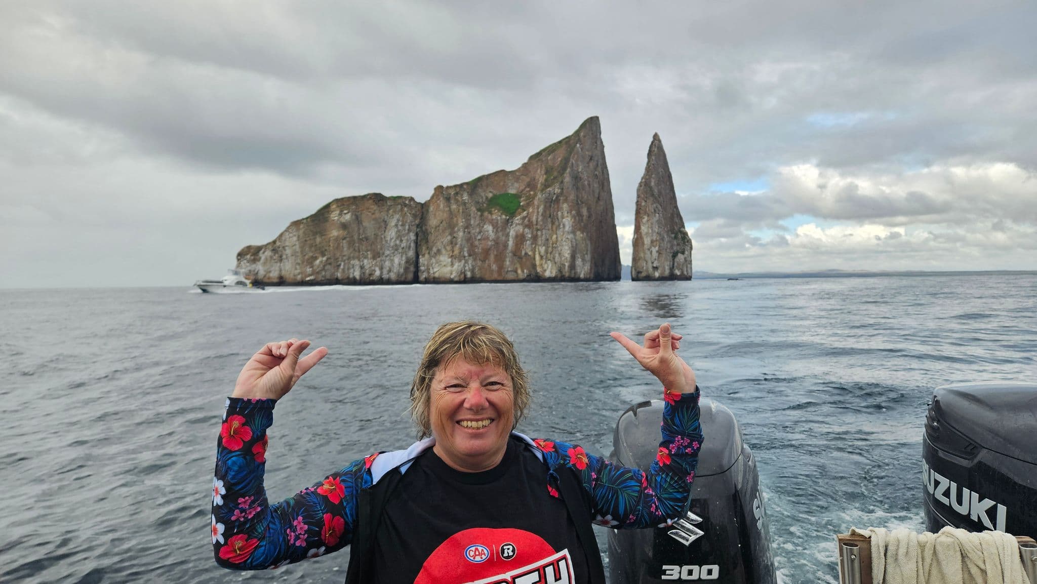 Kicker Rock (León Dormido) sea stacks with a smiling traveler on a boat pointing toward them, Galápagos Islands, Ecuador