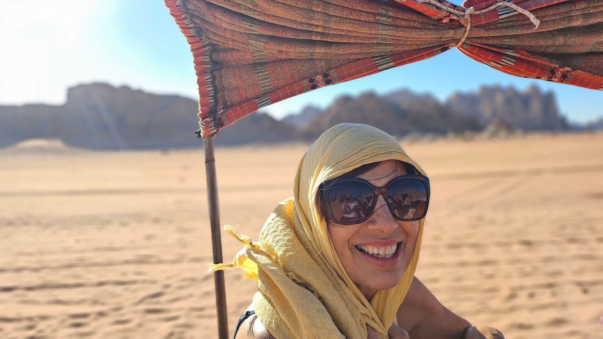 Smiling traveler in a yellow headscarf under a shaded tent in Wadi Rum desert, Jordan.