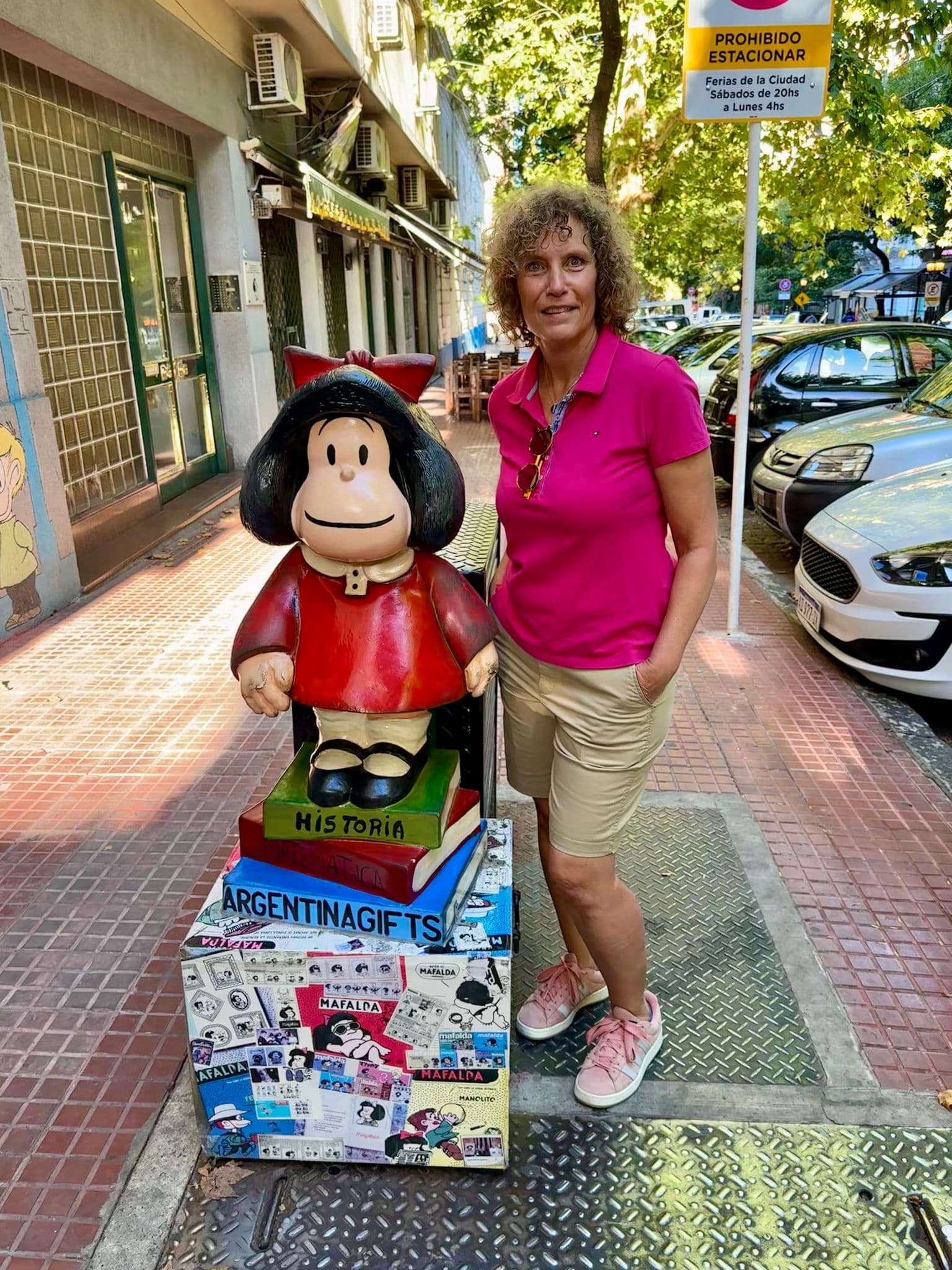 Mafalda statue on a decorated pedestal beside a tourist posing on a Buenos Aires sidewalk, Argentina.