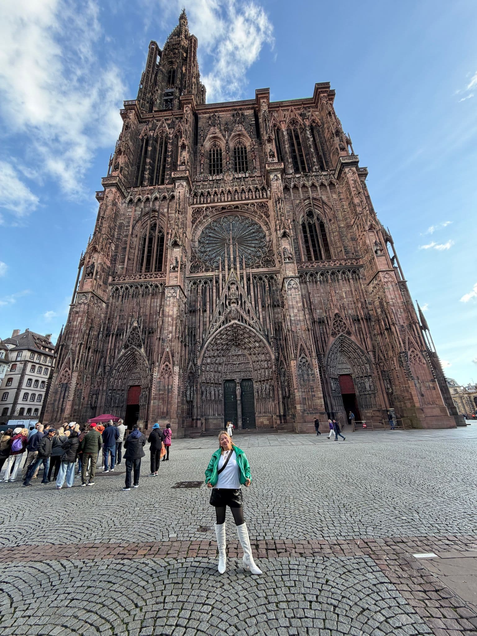 Strasbourg Cathedral (Cathédrale Notre-Dame de Strasbourg) towering over a person posing on the cobbled square in Strasbourg, France.