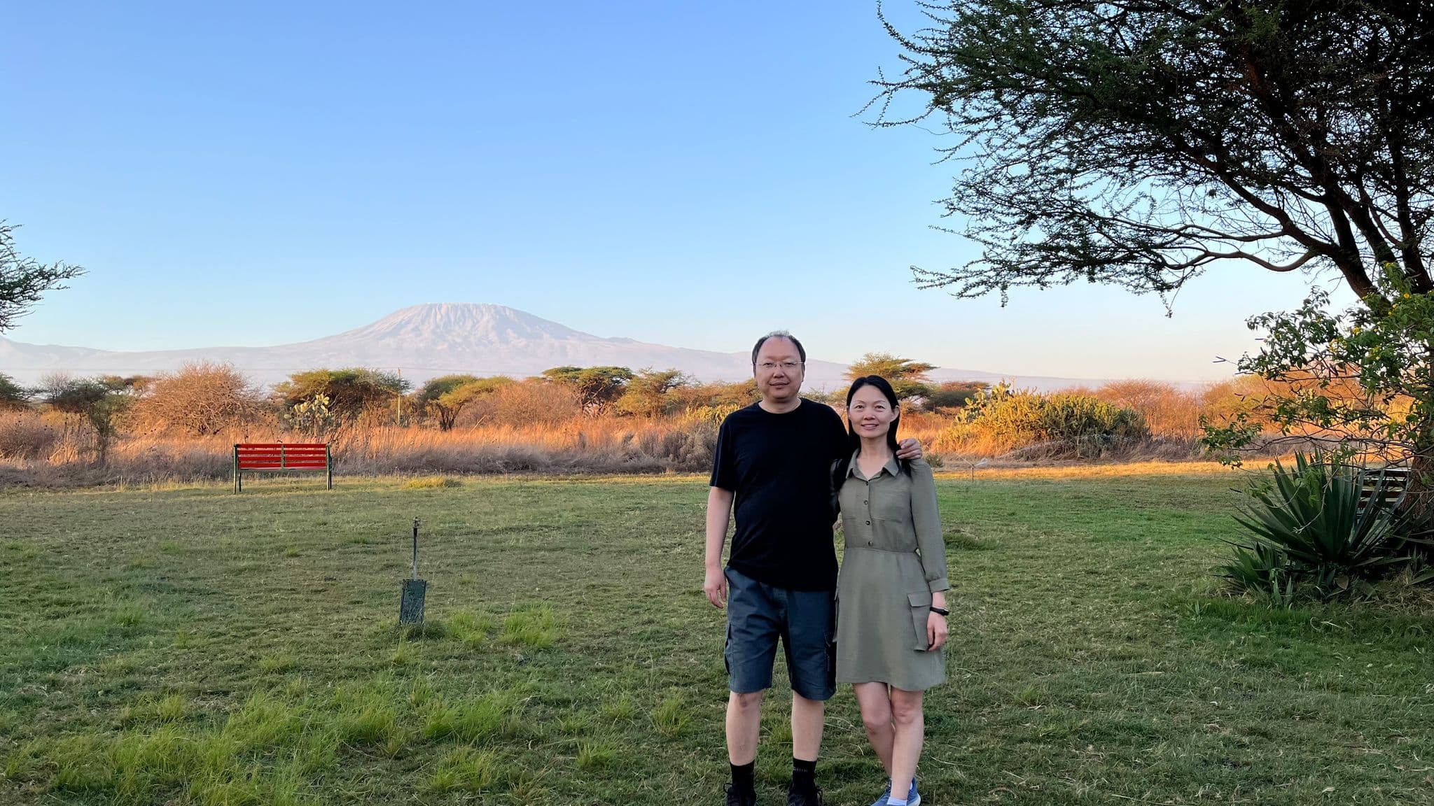 Mount Kilimanjaro rising behind two people standing on a grassy plain at Amboseli National Park, Kenya.