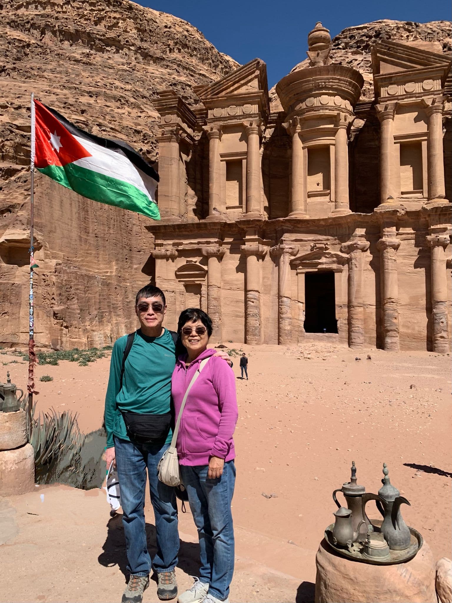 The Monastery (Ad-Deir) at Petra with two travelers posing in front against sandstone cliffs, Jordan.