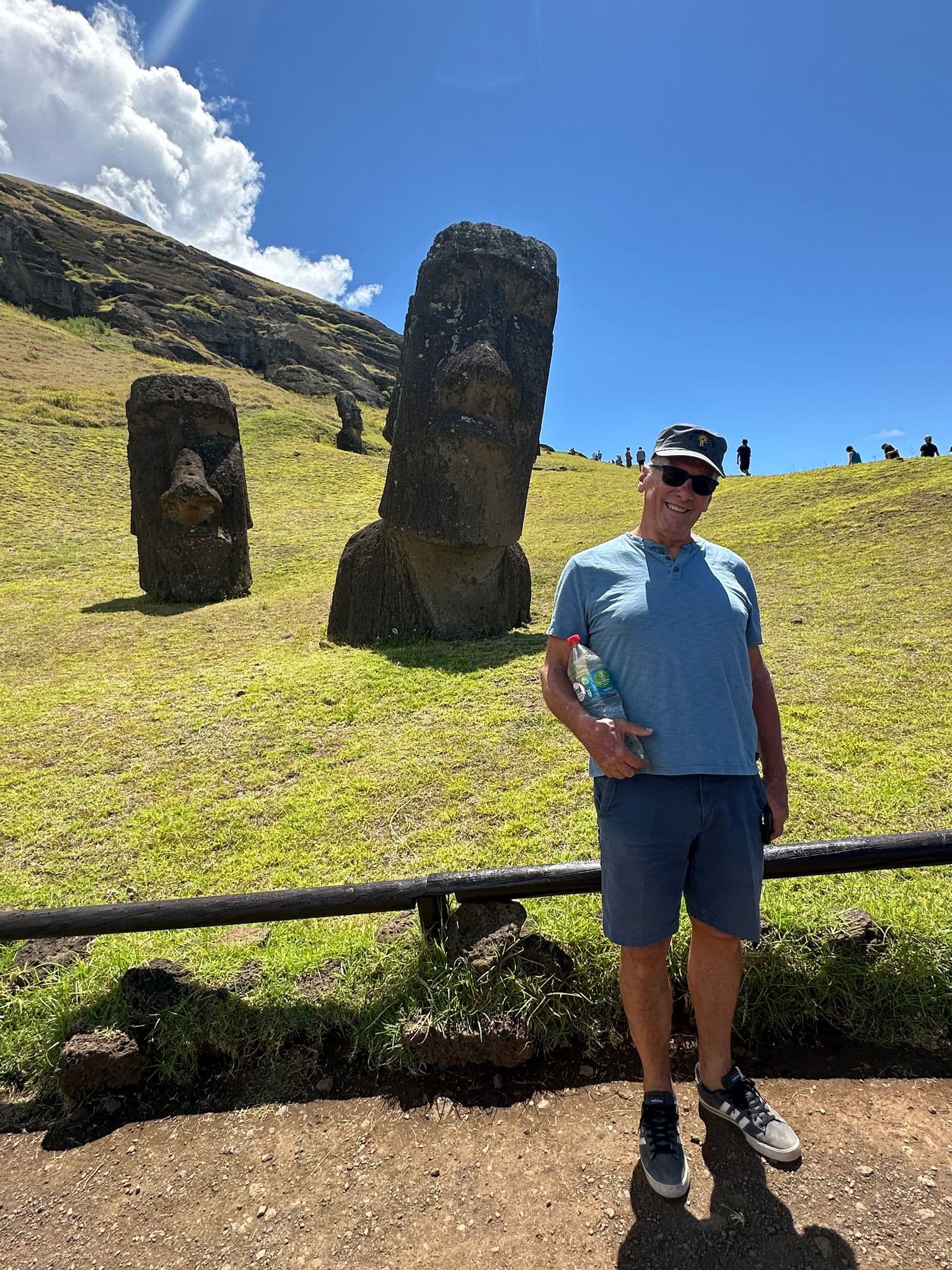Moai statues at Rano Raraku on Easter Island with a smiling tourist posing on the grassy slope, Chile.