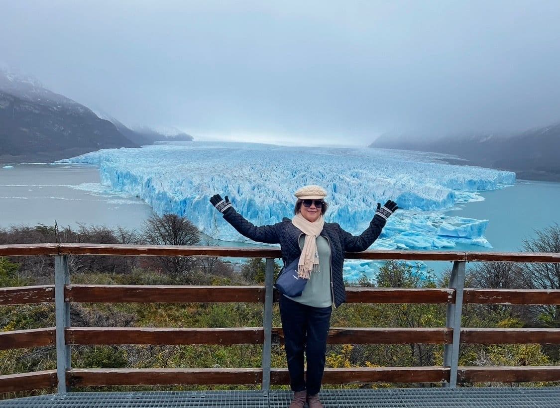 Perito Moreno Glacier with a person standing on a wooden viewing platform with arms outstretched, Patagonia, Argentina.