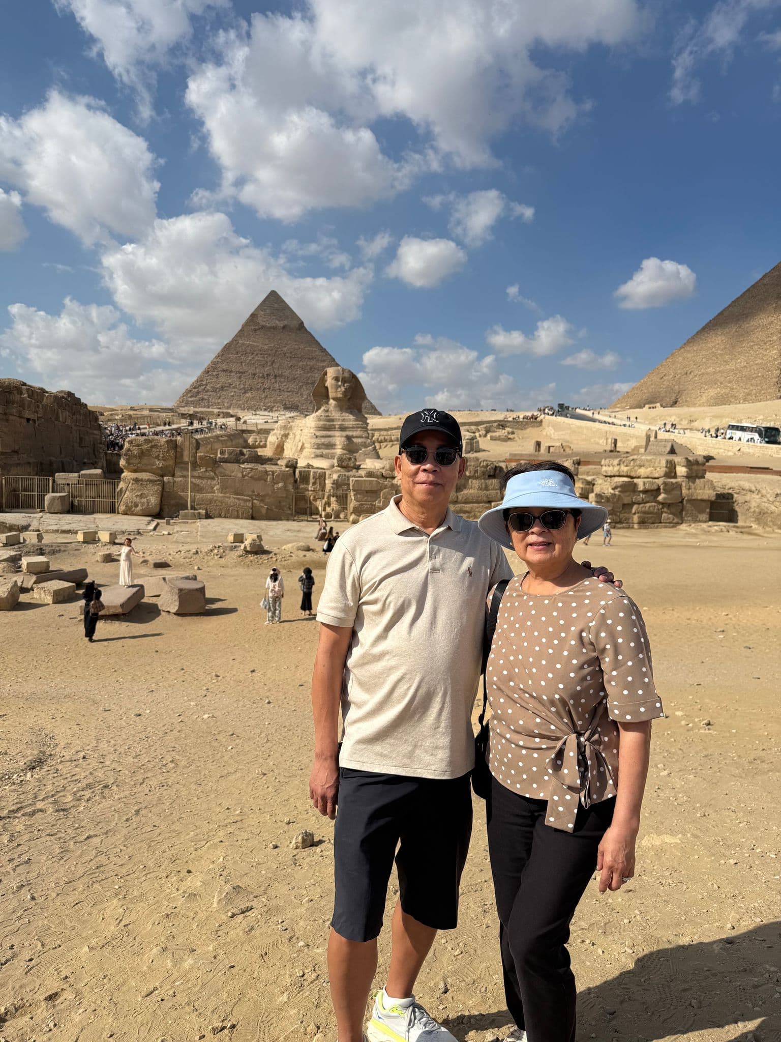 Great Sphinx of Giza with Pyramid of Khafre behind and two tourists posing on the Giza Plateau, Giza, Egypt.