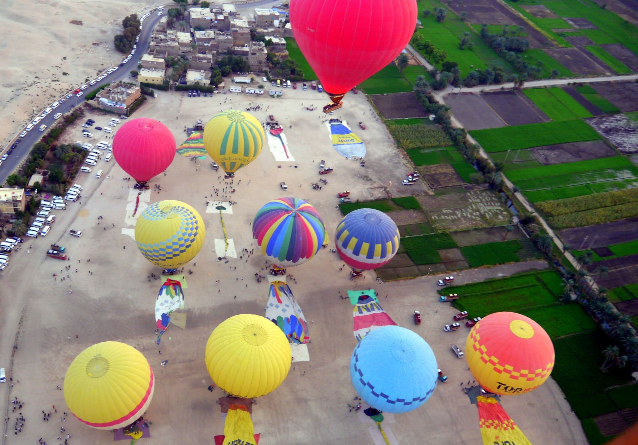 Colorful hot air balloons rising over farmland and desert near Luxor, Egypt during a morning tour.