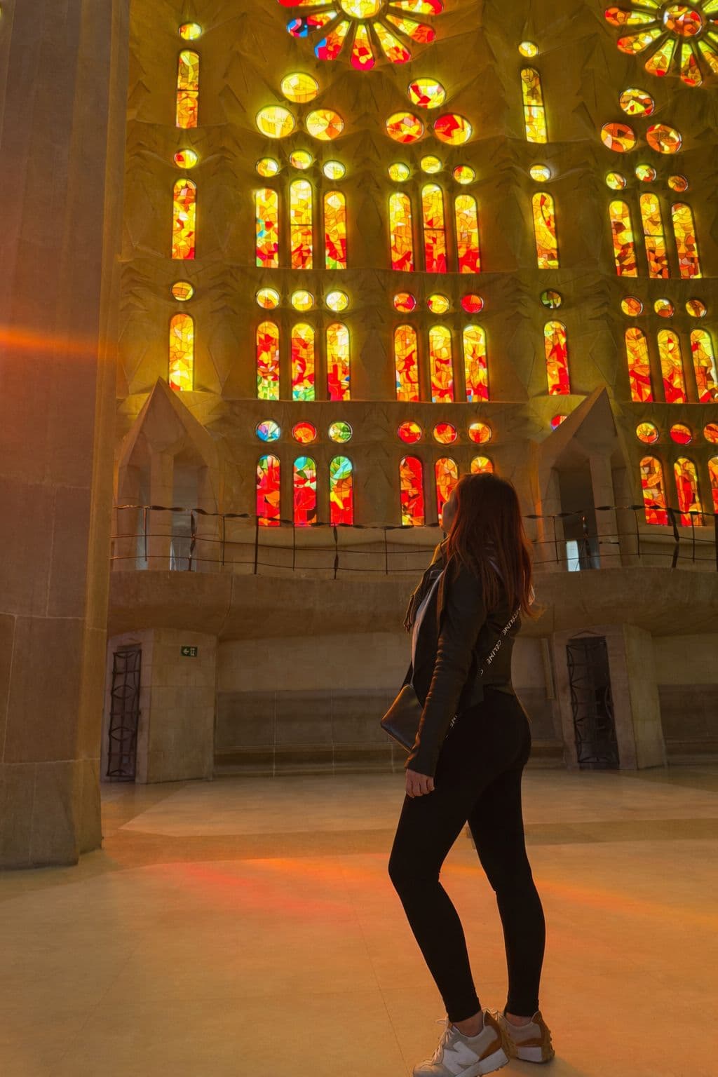 Stained glass windows in La Sagrada Família, Barcelona, Spain, with a visitor standing and looking up as colored light fills the interior.