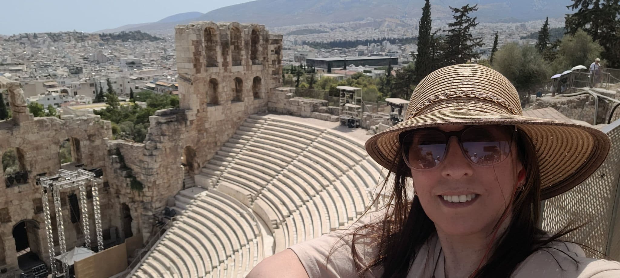 Odeon of Herodes Atticus amphitheatre with a woman taking a selfie wearing a straw hat and sunglasses on the Acropolis, Athens, Greece