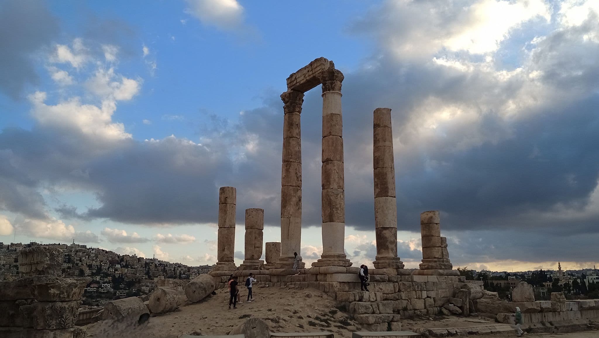 Temple of Hercules ruins at the Amman Citadel with visitors among tall columns under a dramatic cloudy sky, Amman, Jordan.