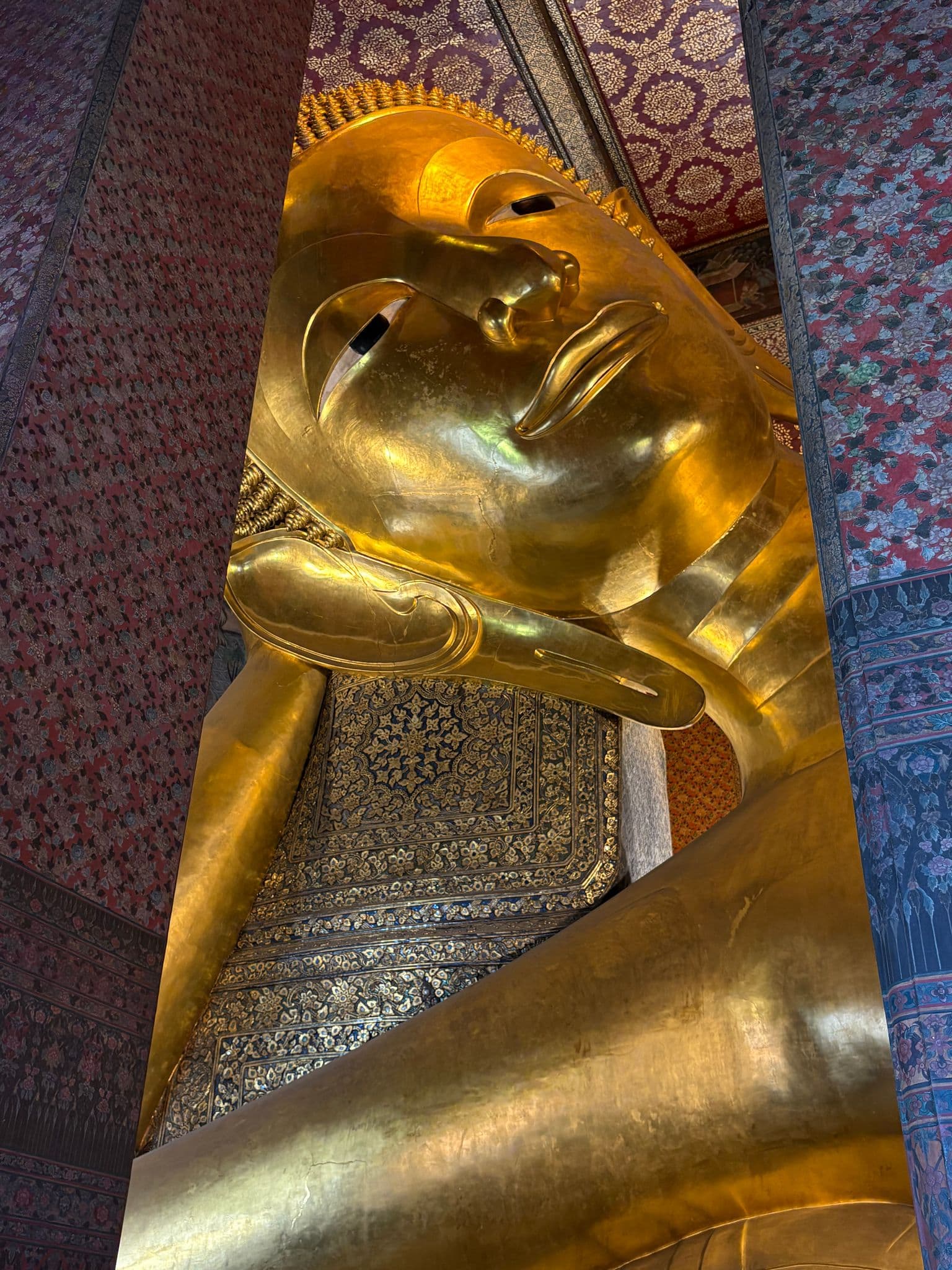 Reclining Buddha statue at Wat Pho inside an ornately patterned temple in Bangkok, Thailand.