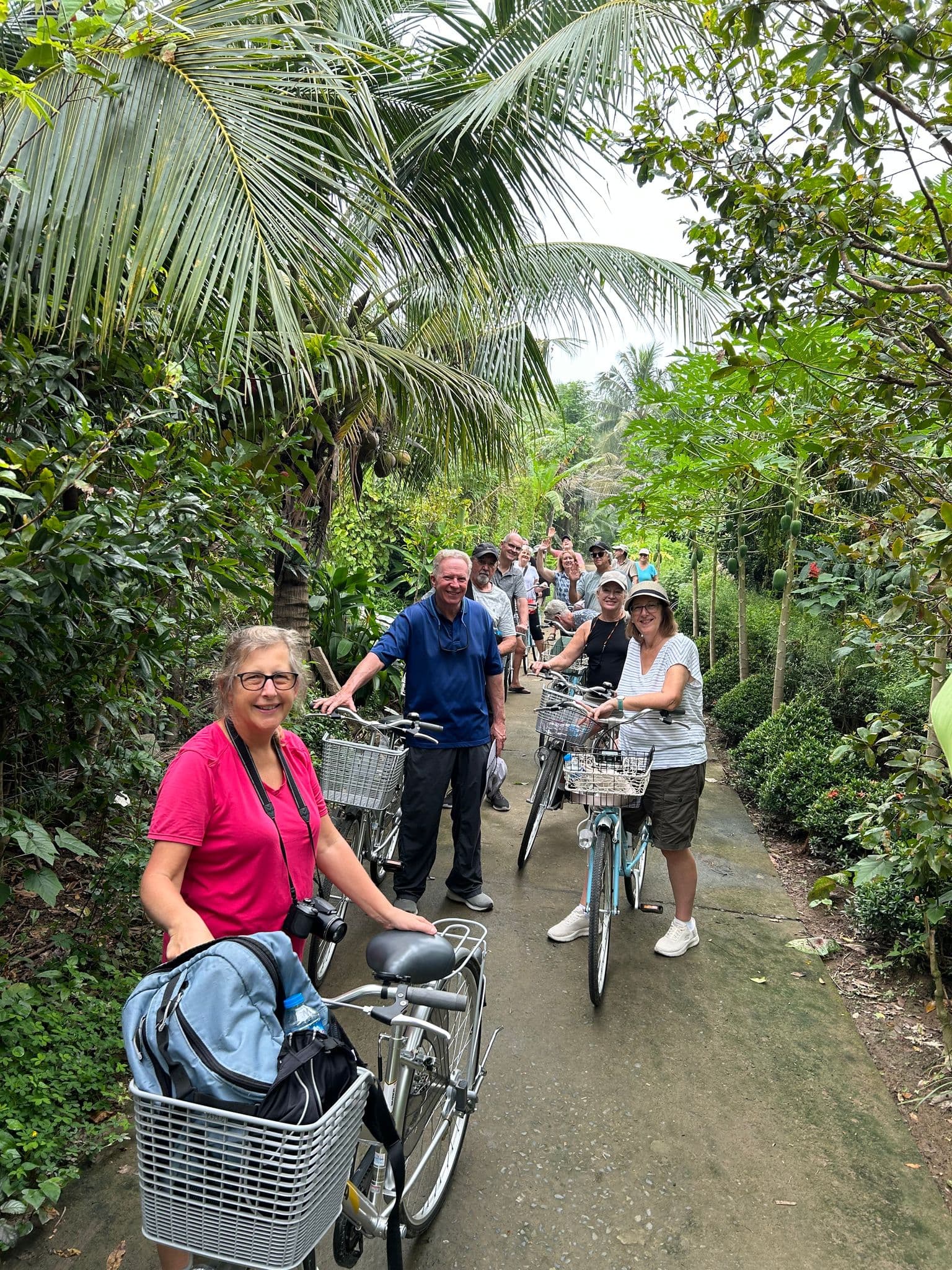 Group of travelers with bicycles standing on a palm-lined path on an island in the Mekong Delta, Vietnam.