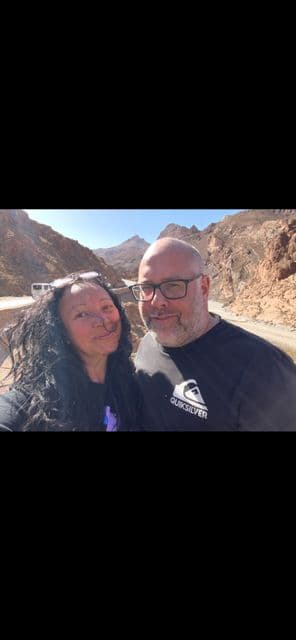 Todra Gorge cliffs with two travelers taking a selfie on a roadside in the rocky valley near Todra Gorges, Morocco.