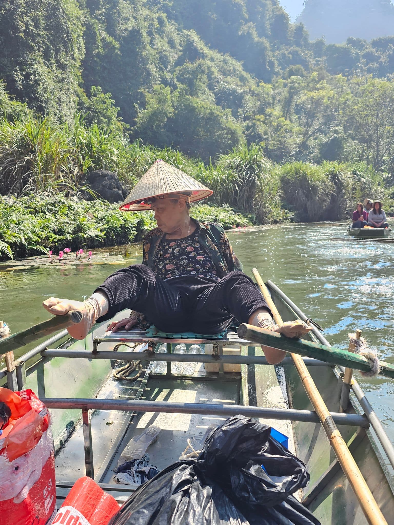 Tam Coc river framed by limestone karsts with a local rower using her feet on a small boat, Ninh Binh, Vietnam