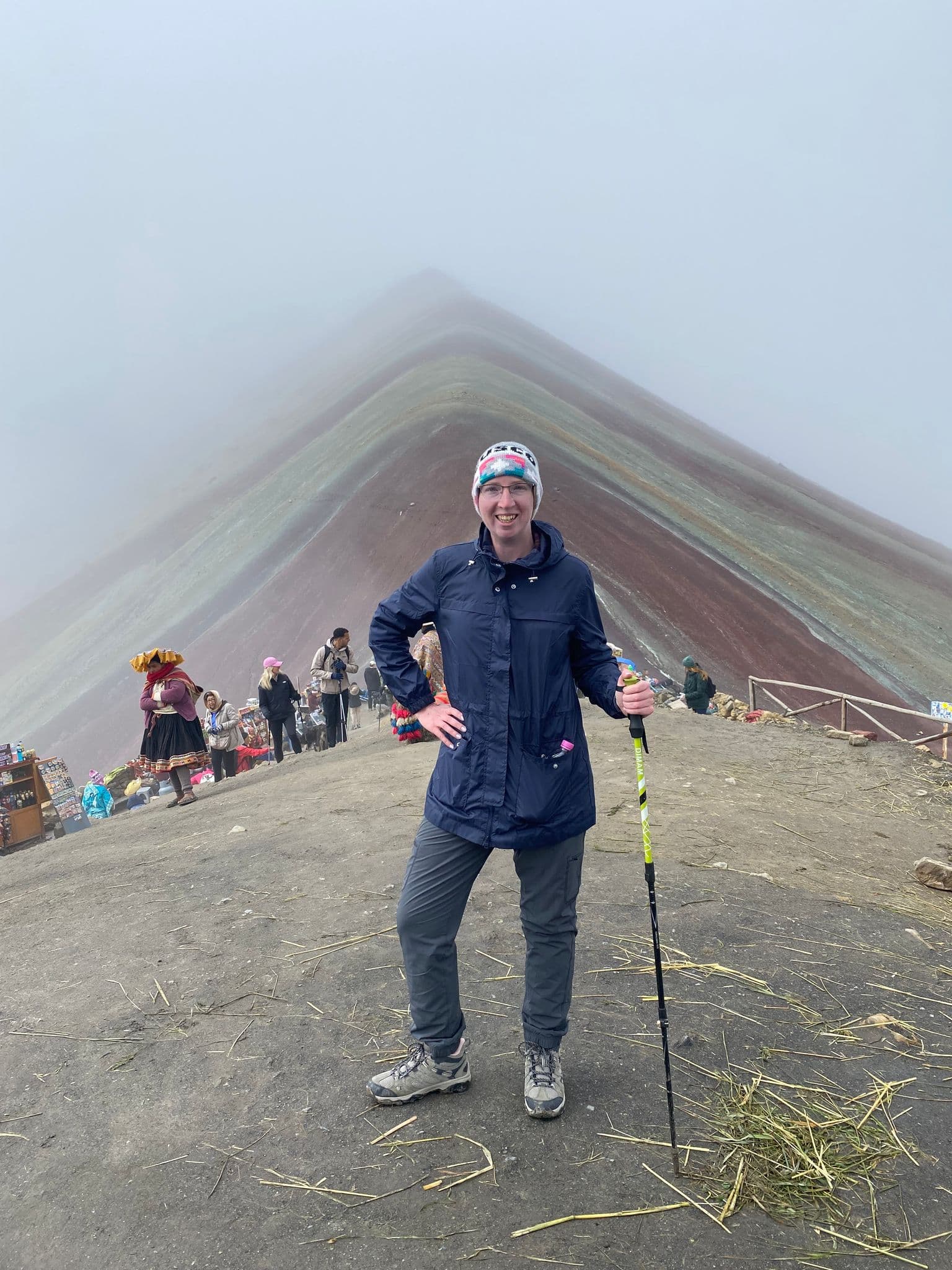 Vinicunca (Rainbow Mountain) ridge with a hiker standing at the summit holding a trekking pole, Cusco, Peru.