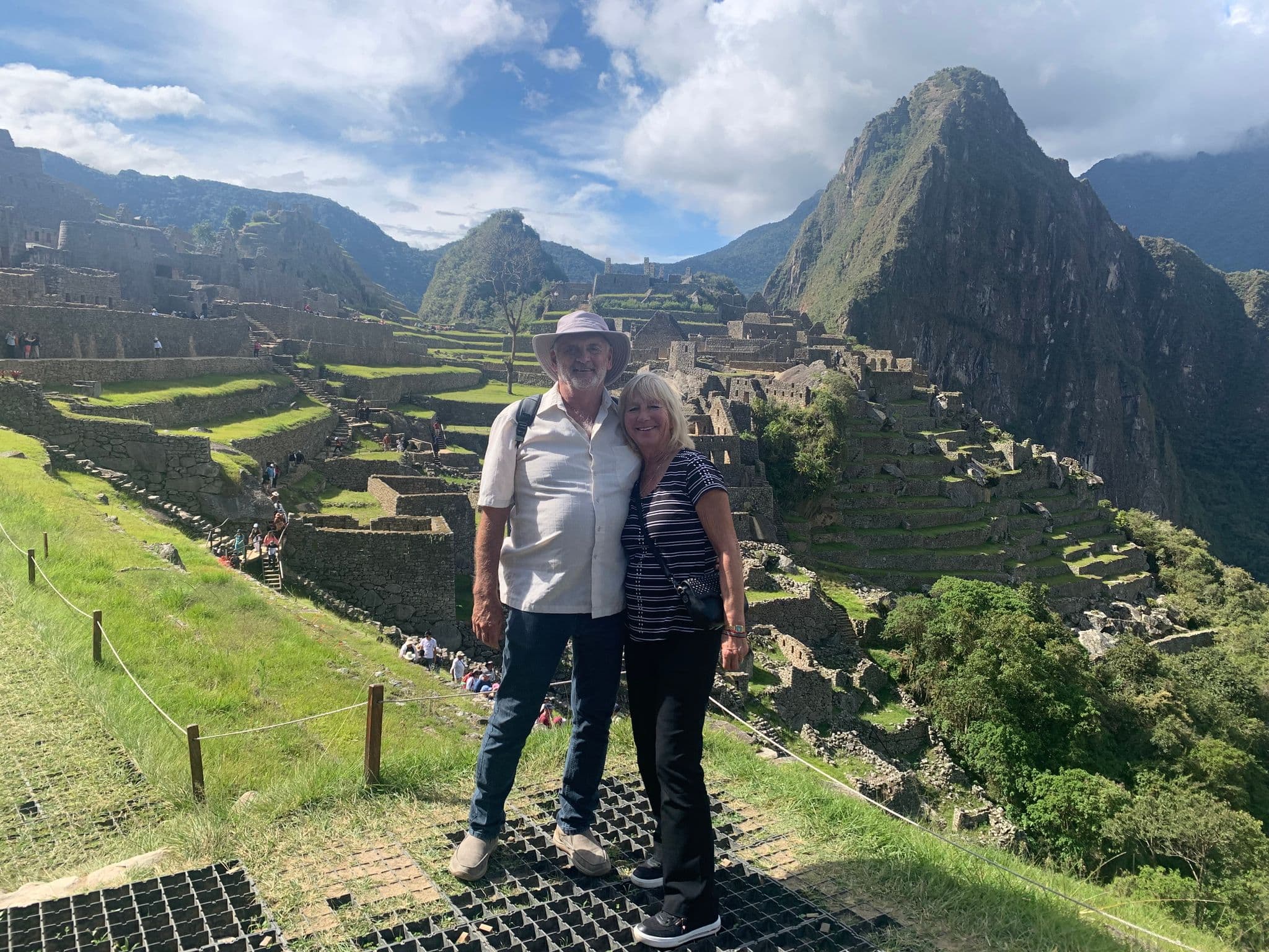 Machu Picchu ruins with two travelers posing in the foreground on terraces, Cusco Region, Peru.
