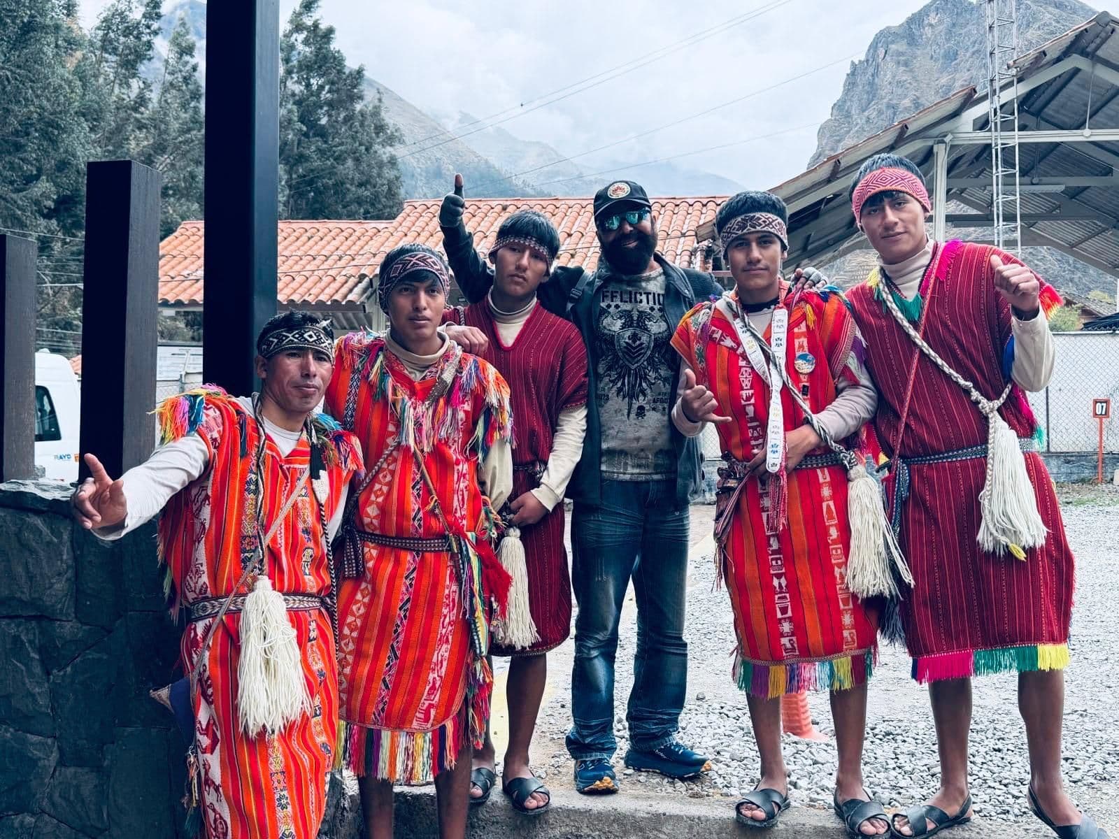 Group of men in red Andean clothing posing with a traveler by mountains in the Peruvian Andes, Peru.