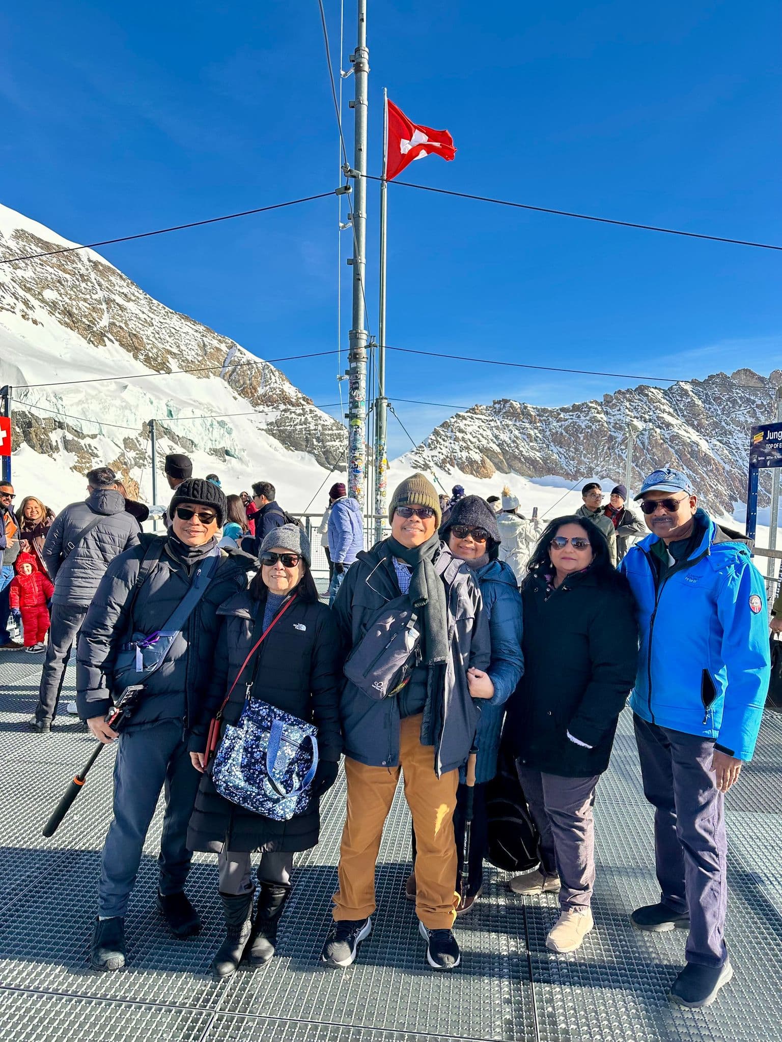 Jungfraujoch viewing platform with a group of travelers posing on a sunny day against snow-covered Bernese Alps, Switzerland