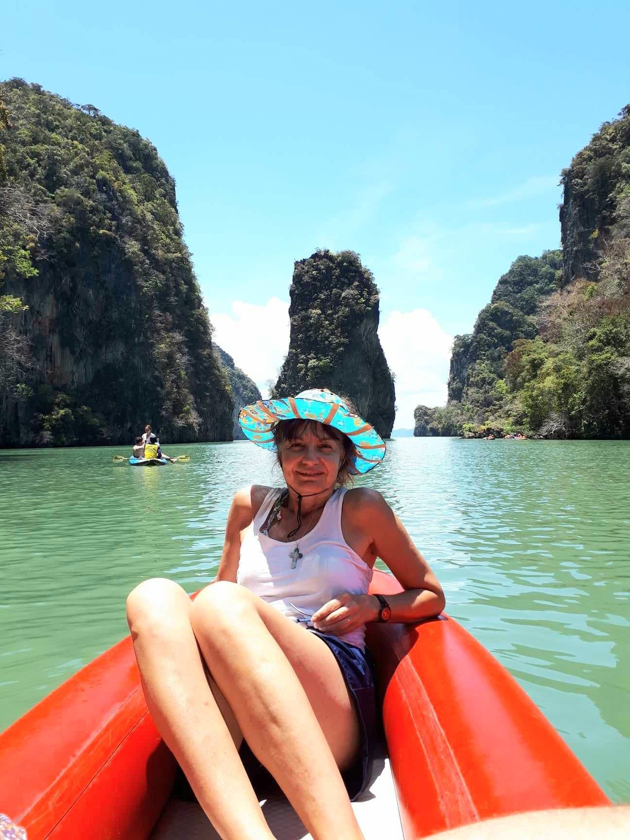 James Bond Island (Koh Tapu) between limestone cliffs, with a woman seated in a red kayak on green water, Phang Nga Bay, Thailand.