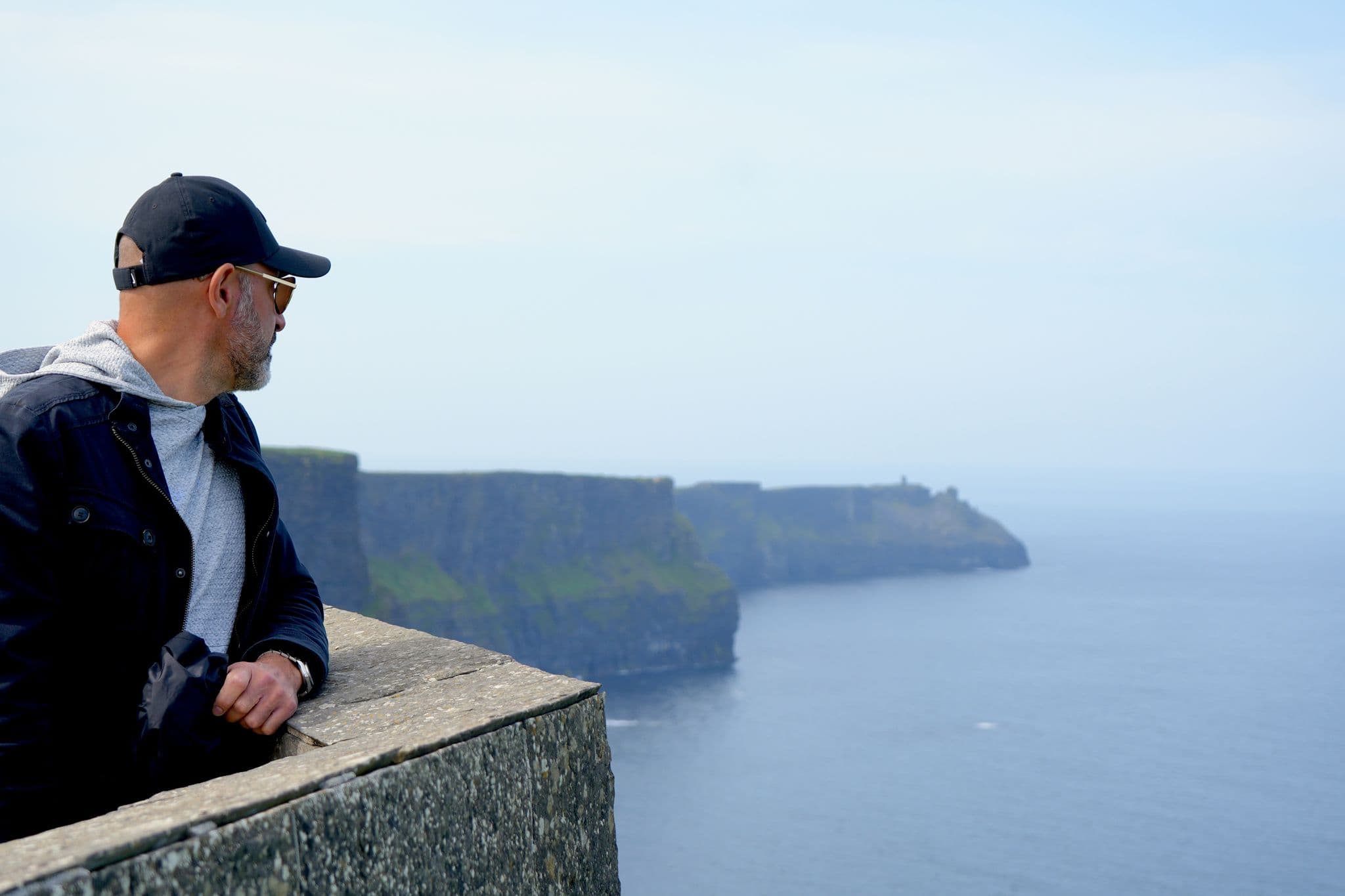 Cliffs of Moher sea cliffs with a man leaning on a stone railing looking out over the Atlantic, County Clare, Ireland.