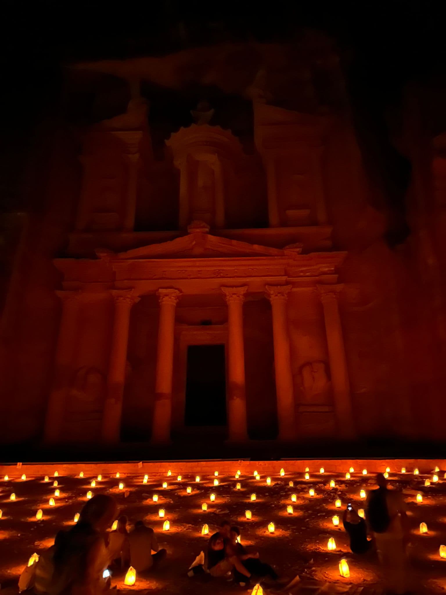 Al-Khazneh (the Treasury) at Petra lit by dozens of ground candles, with visitors seated in the foreground, Jordan.